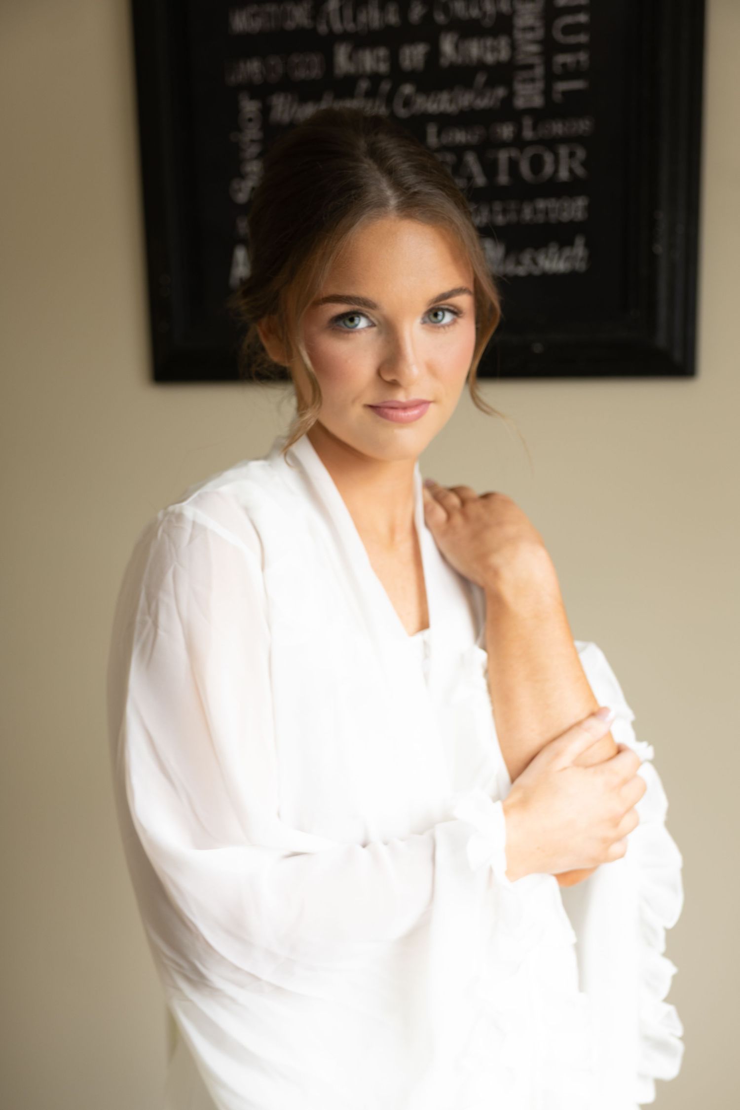 Young woman in white robe with elegant updo hairstyle and natural makeup poses gracefully indoors.