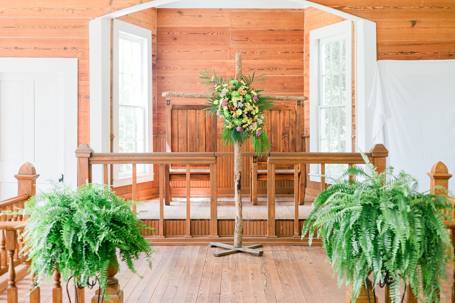 Elegant wedding chapel interior with wooden pews, ferns, and a floral arrangement at the altar.