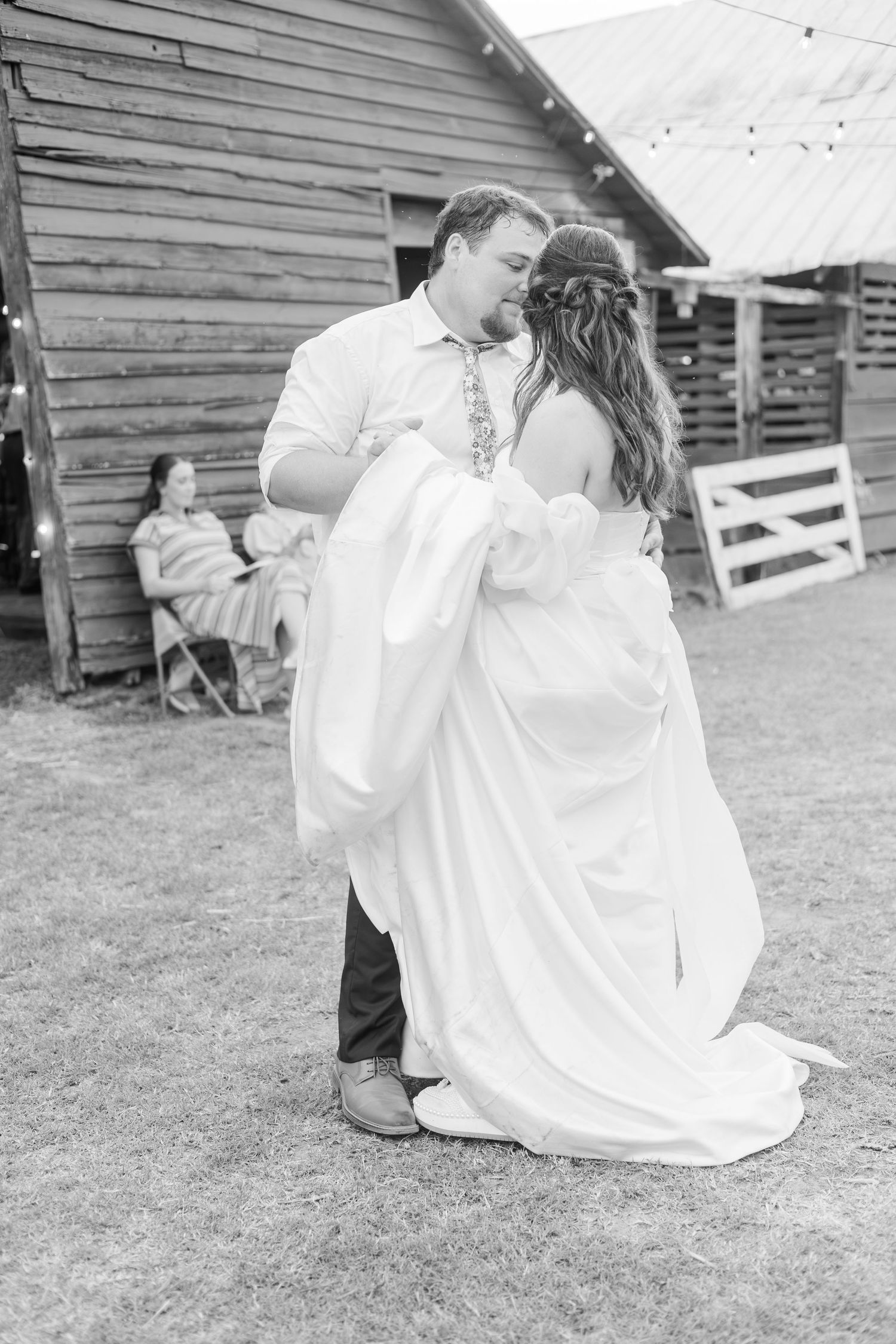Black and white photo of bride and groom sharing first dance outside rustic barn wedding venue.