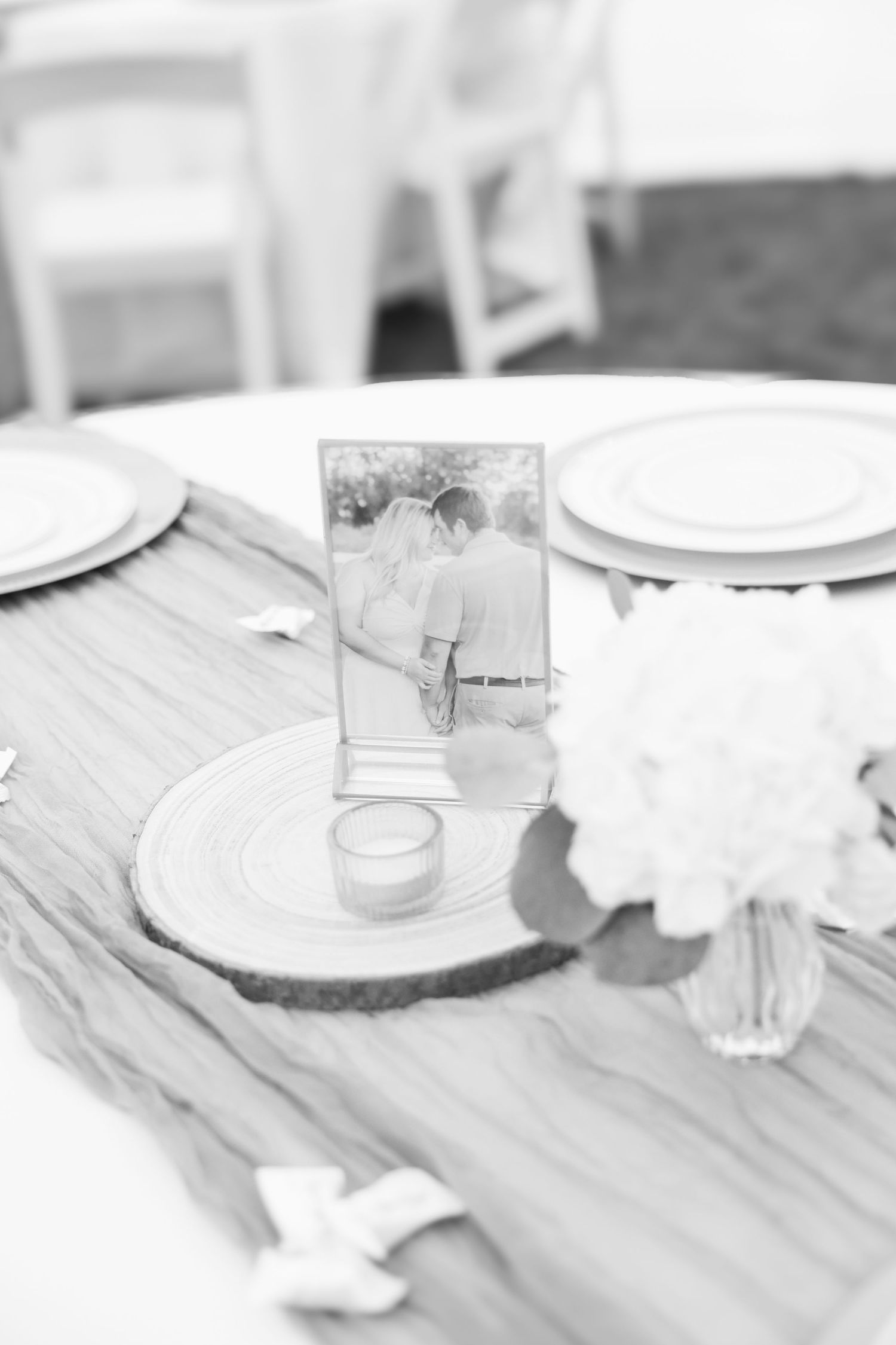 Black and white wedding table setting with framed couple photo, wood slice charger, floral centerpiece, and elegant place settings.