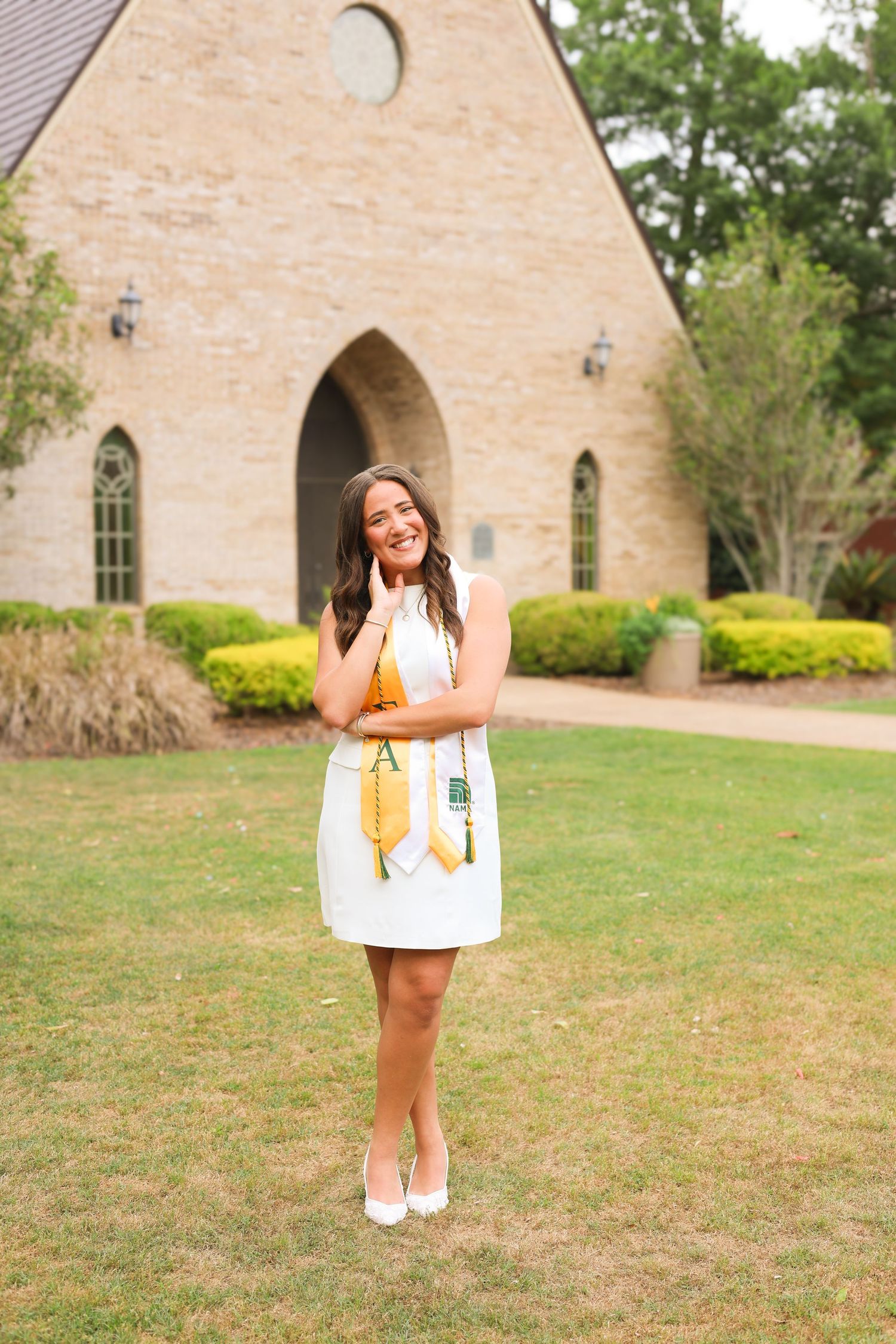 Graduation photos taken in front of stone church building with landscaped grounds.