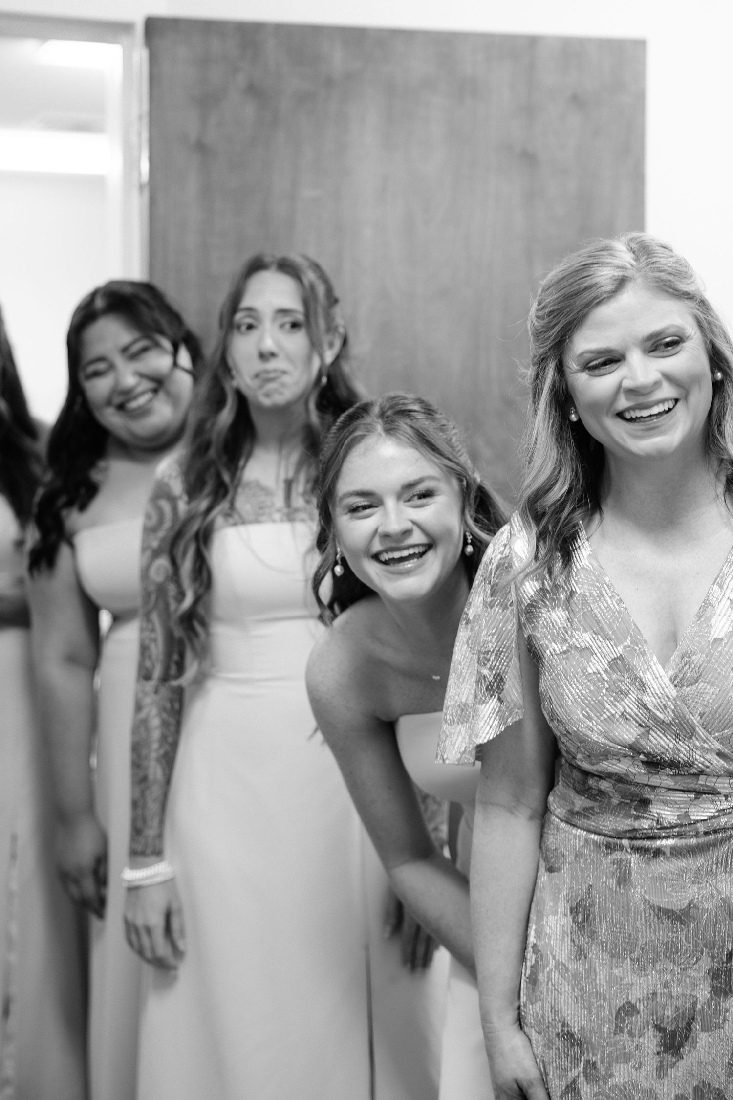 Black and white photo of four bridesmaids laughing and posing together in elegant dresses at a wedding.