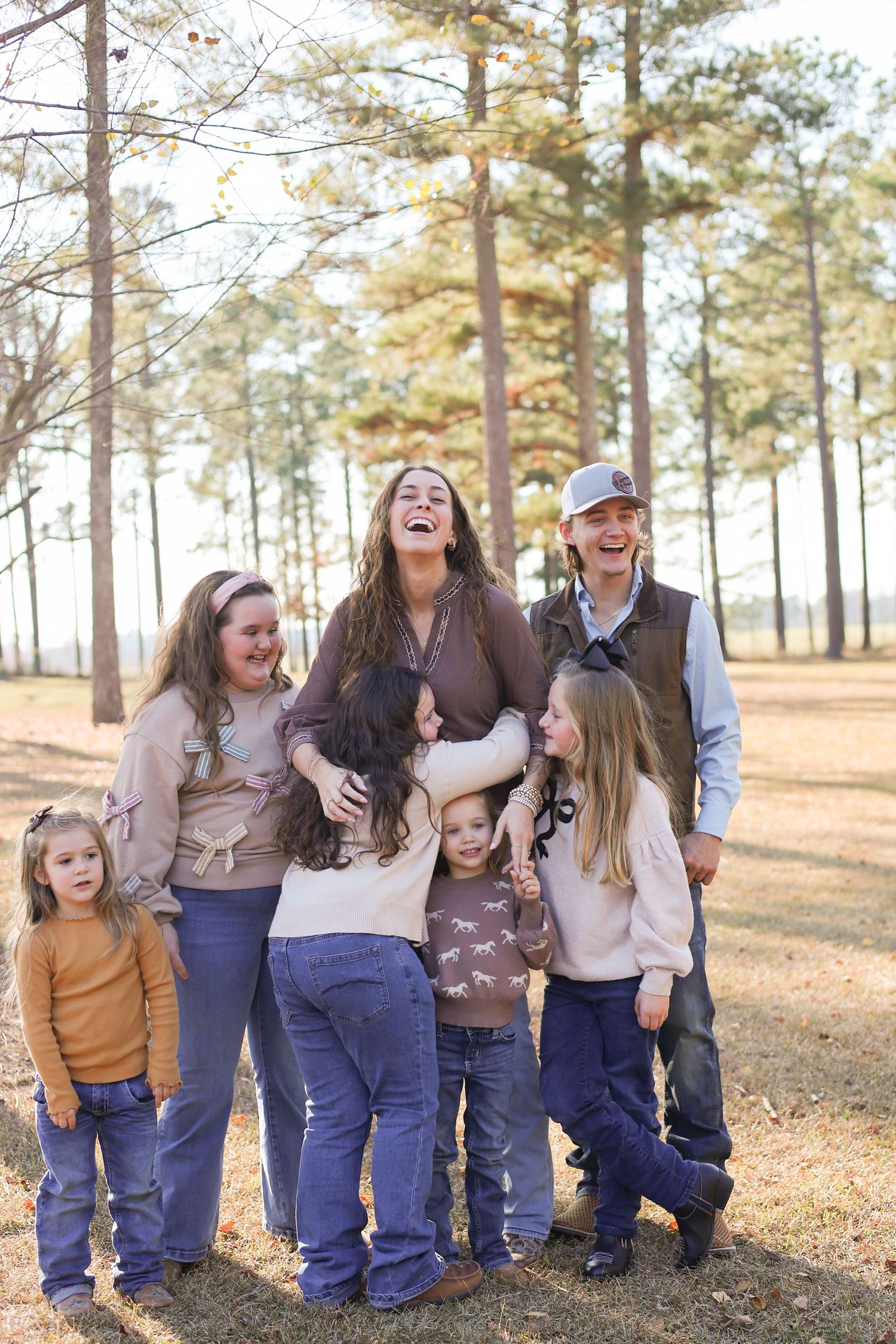 Happy family with children laughing together outdoors among tall pine trees during a fall day.