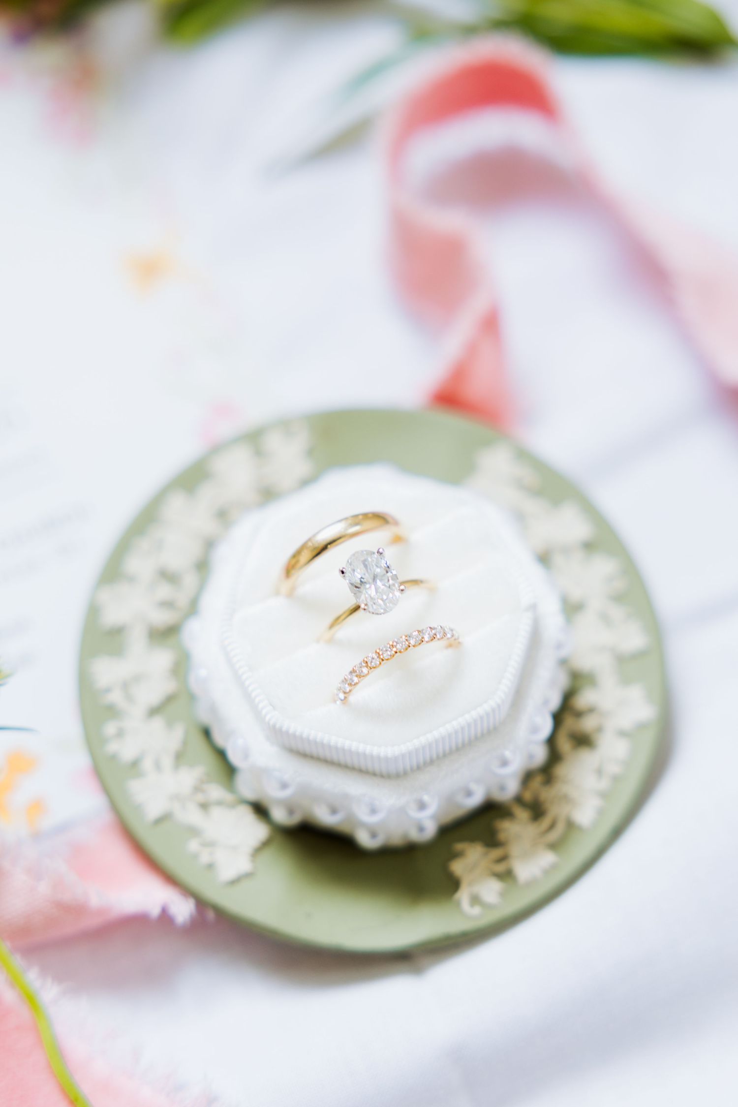 Gold engagement ring with diamond solitaire and wedding band displayed in white velvet ring box on green plate.