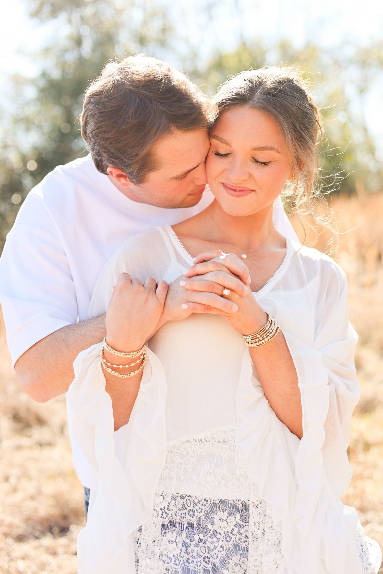 A romantic outdoor photoshoot showing tender moments between a couple in white clothing against a sunlit natural backdrop.