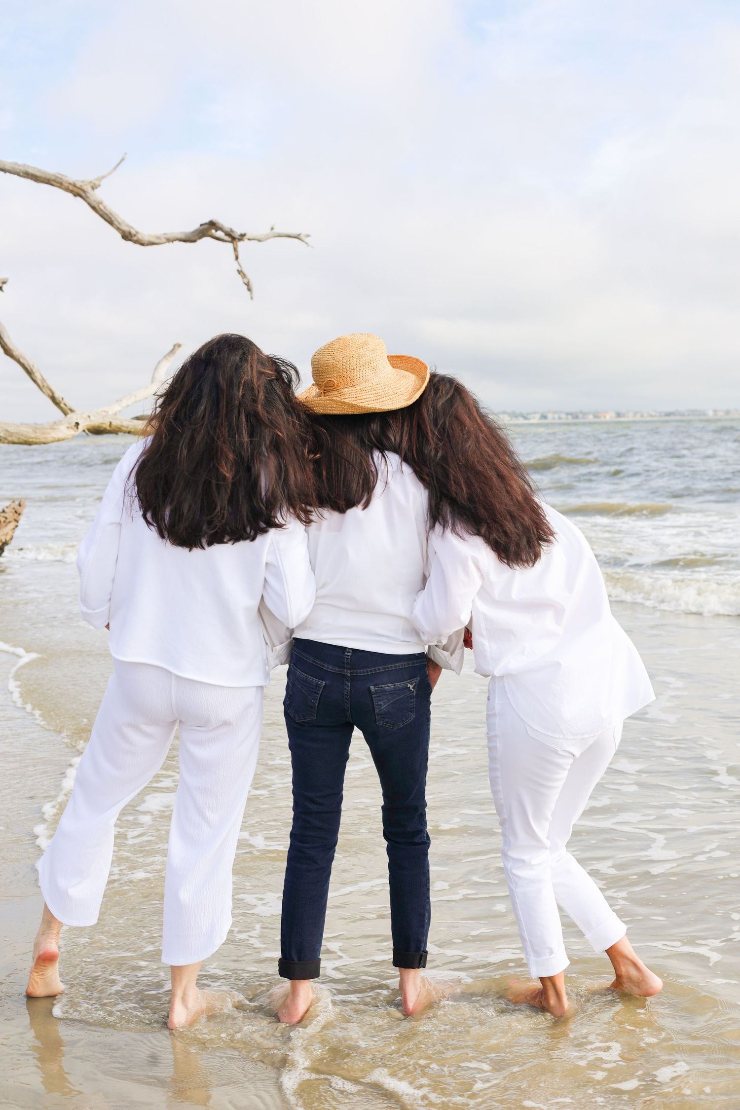 Four people in white shirts and jeans walk along the beach shoreline with their backs to the camera.