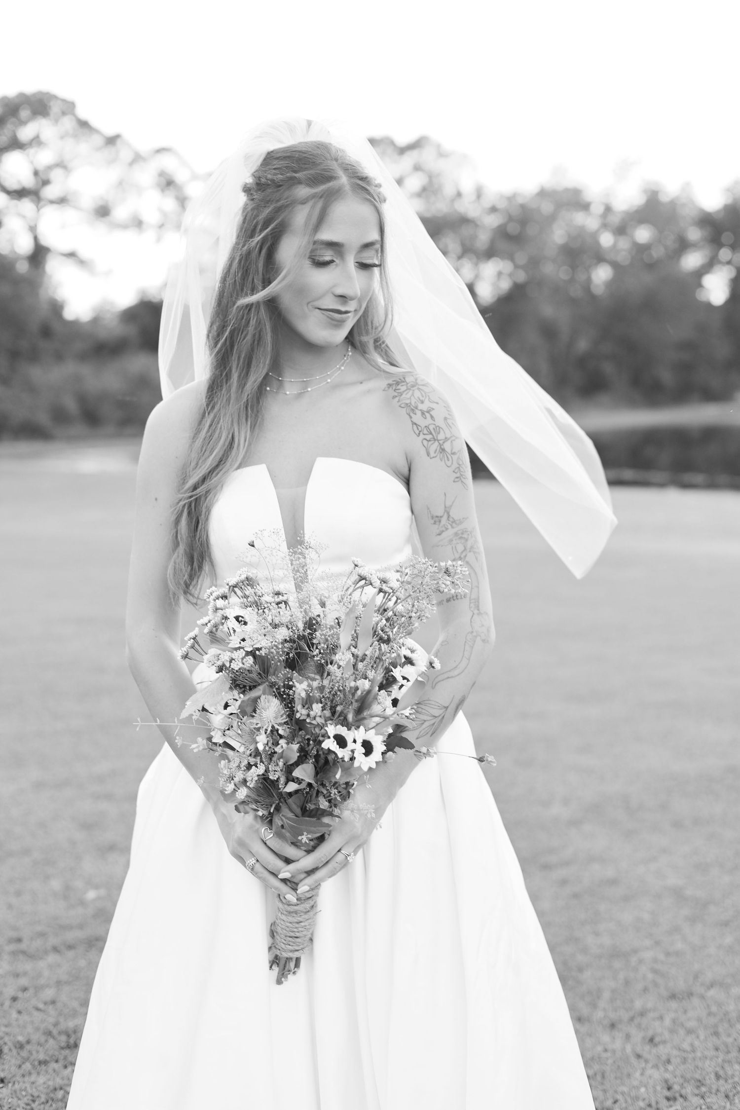 Black and white portrait of bride holding wildflower bouquet in an outdoor setting.