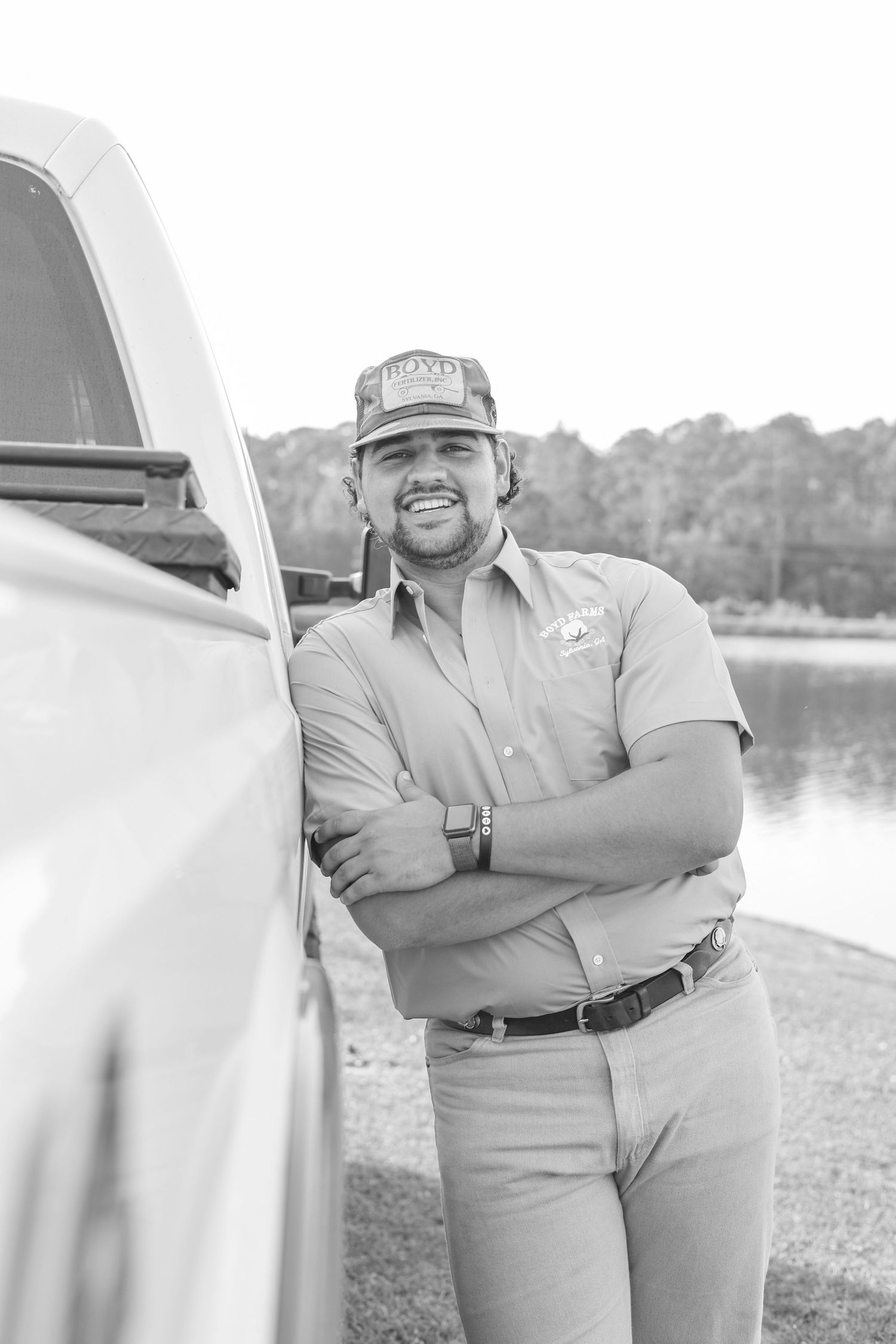 Black and white portrait of person in work attire leaning against truck.