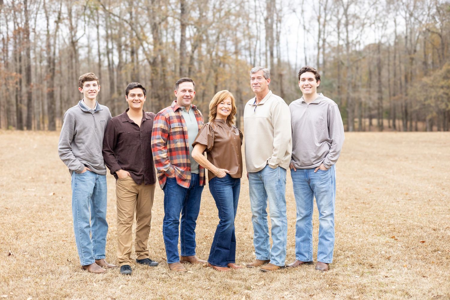 A group of six people in casual clothing standing together in a field with bare trees in the background.