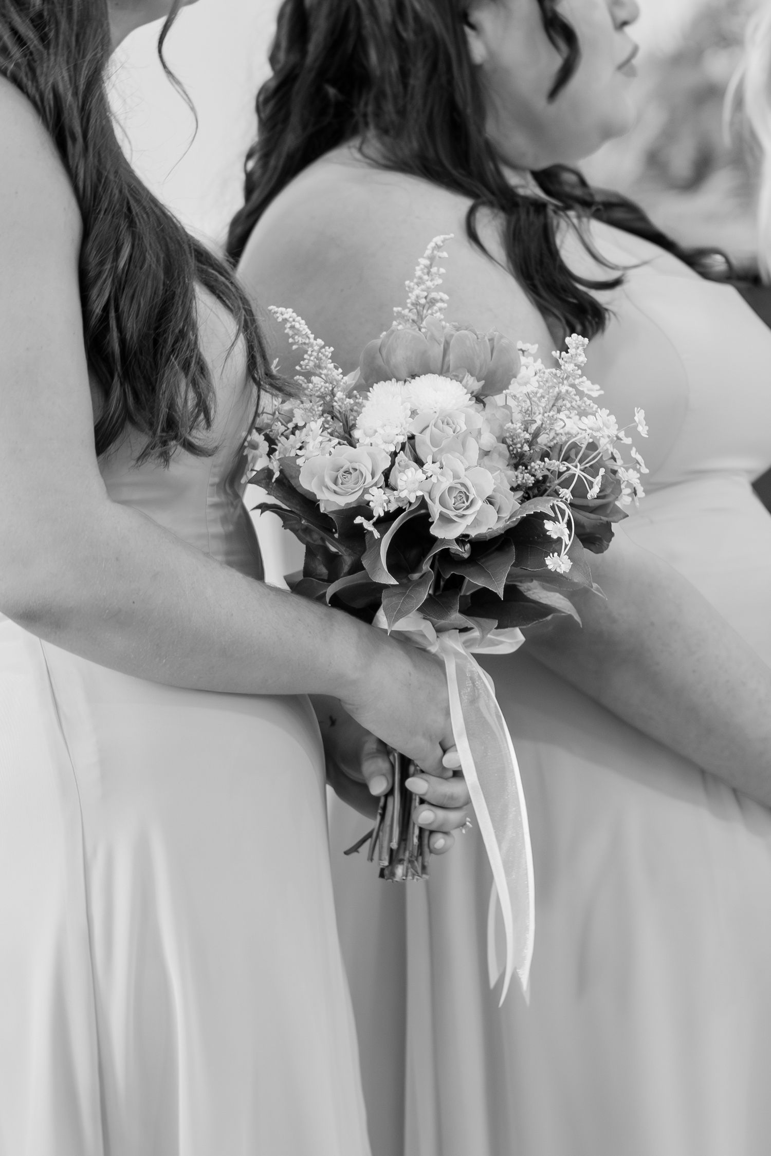 Black and white close-up of bridesmaid holding a bouquet of roses and wildflowers in flowing gown.
