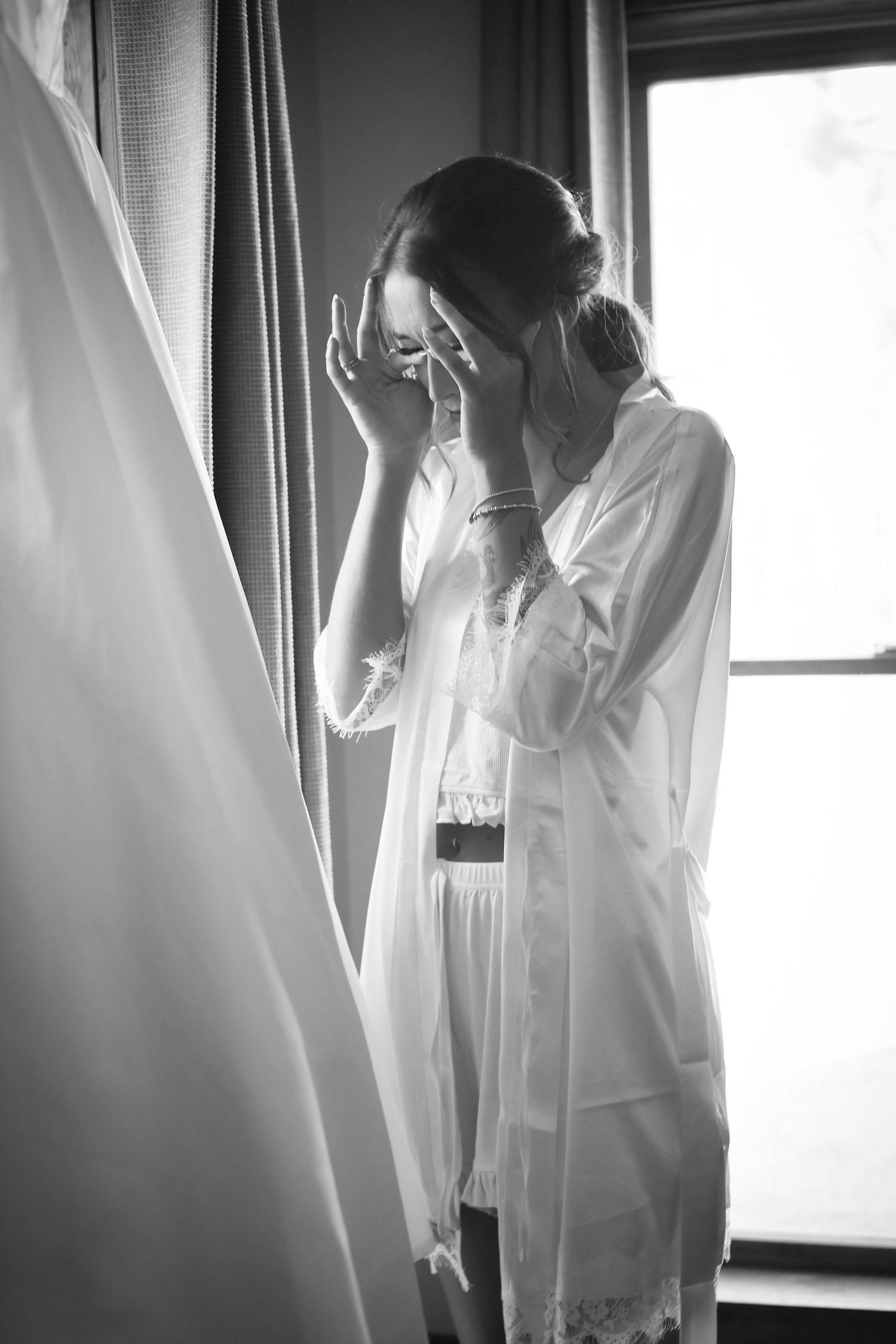 Emotional wedding morning moment captured in black and white near a window.