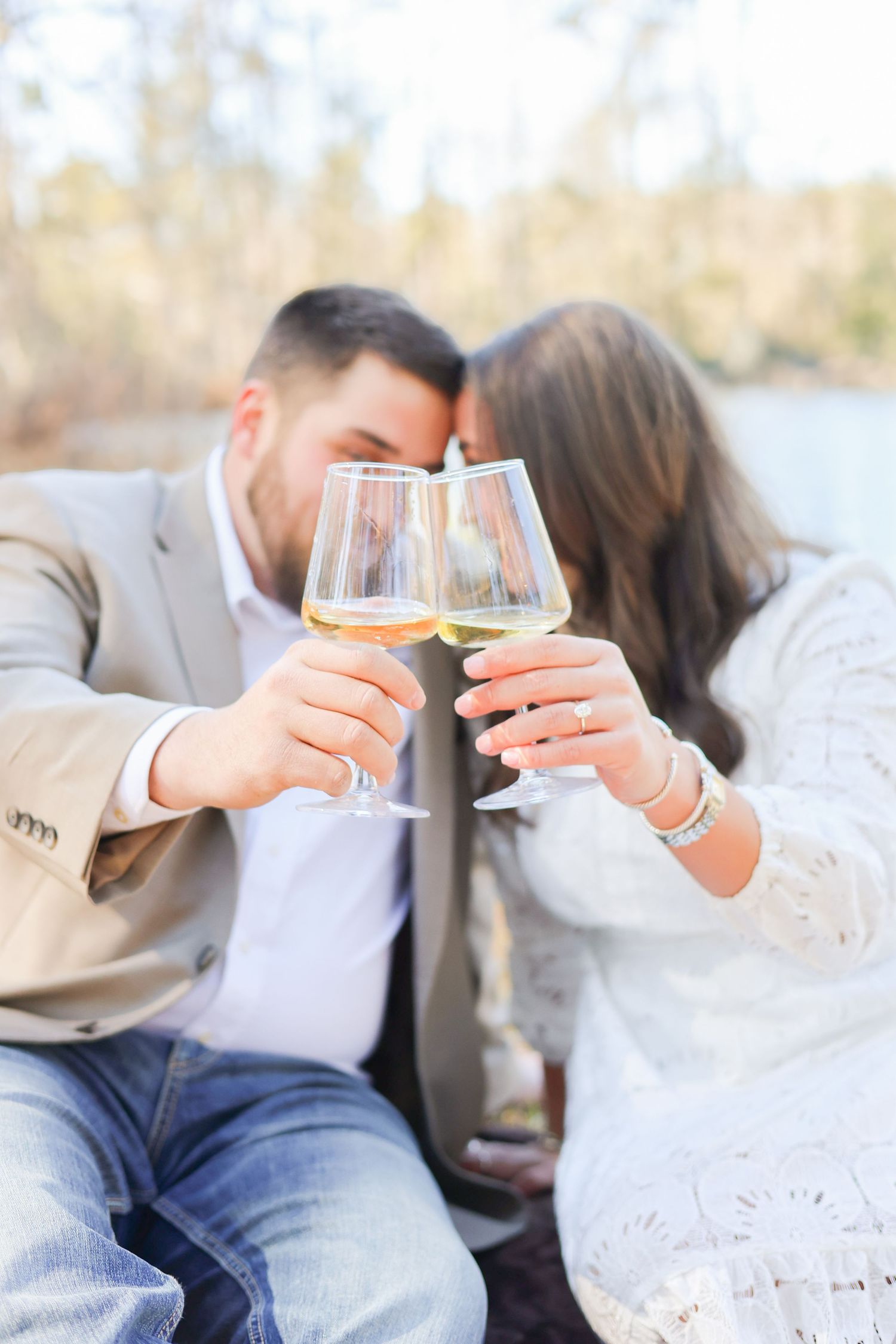 A couple toasting with wine glasses while sitting outdoors on a sunny day.
