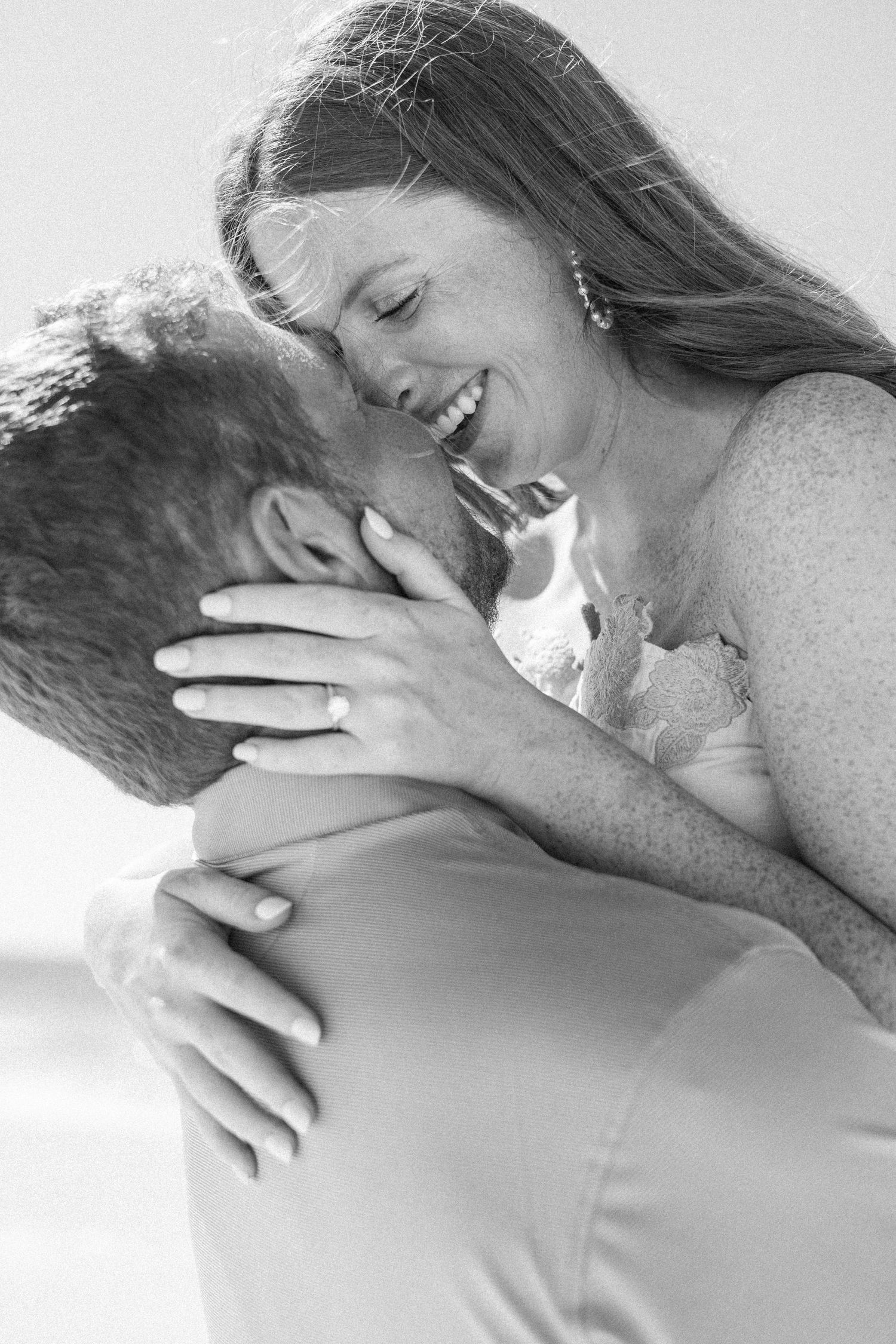 Black and white photo of a smiling bride being lifted by groom, sharing a romantic moment outdoors.
