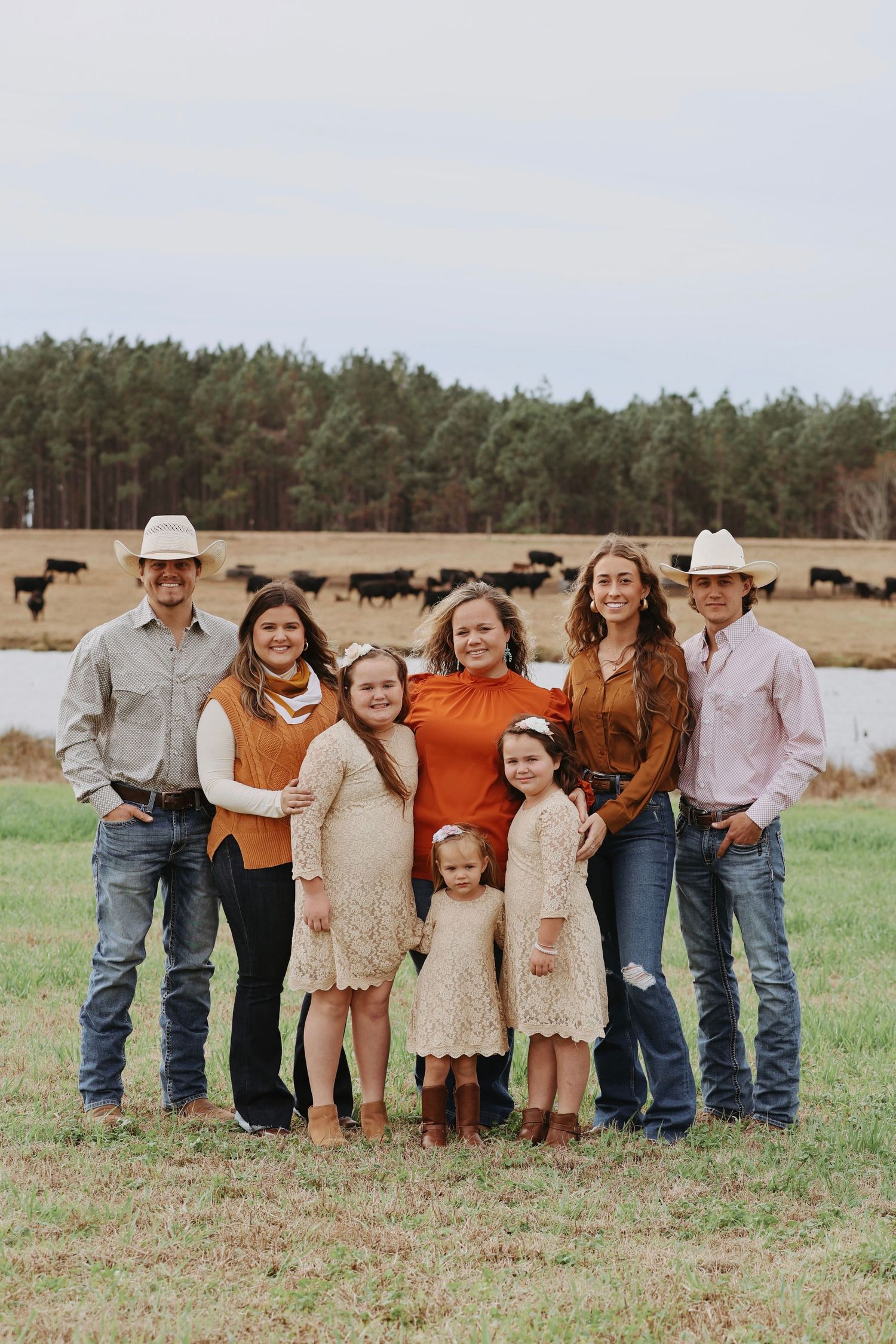 Large family group in western attire poses together in rustic field setting.