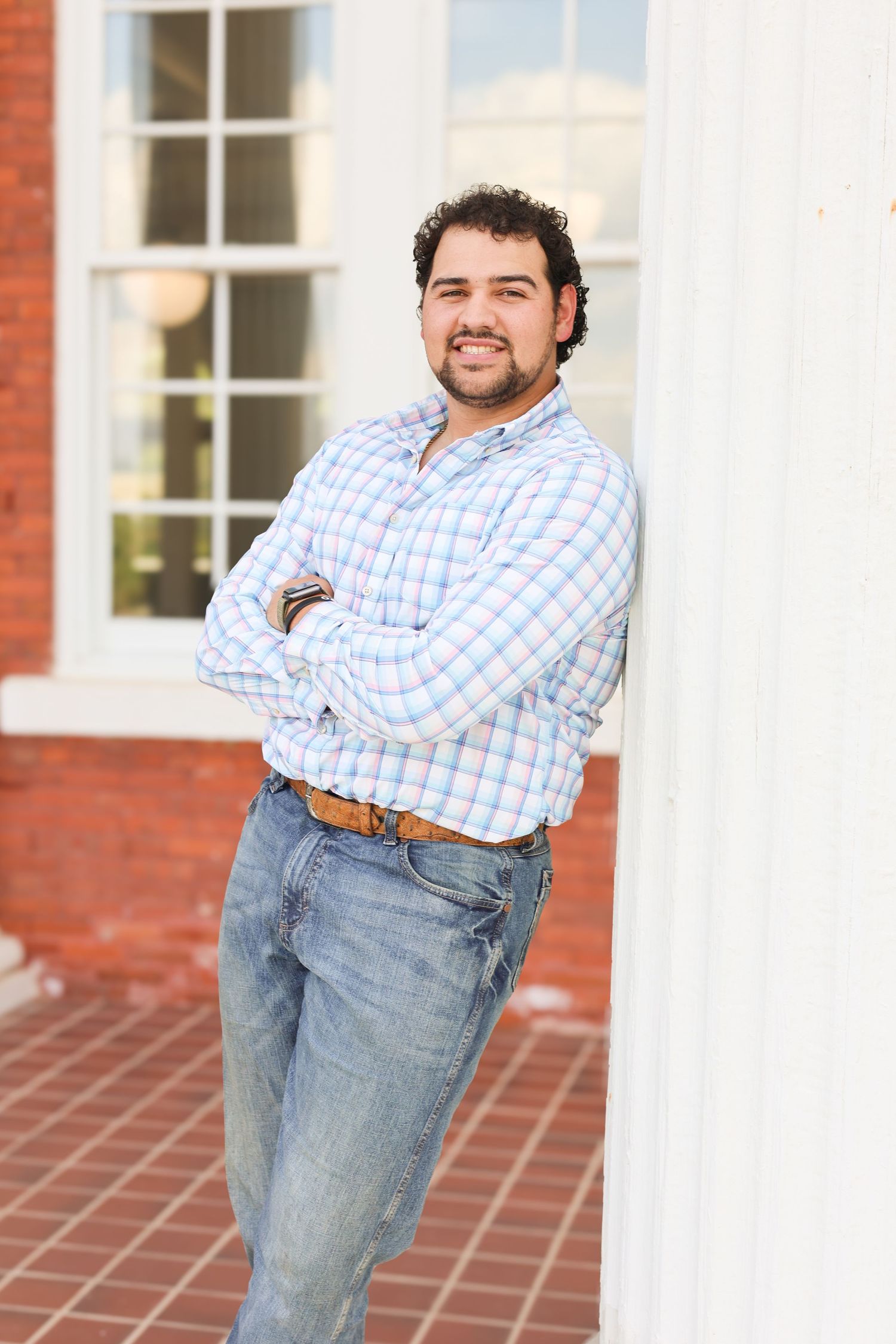 Person in checkered shirt poses casually against white column outdoors.