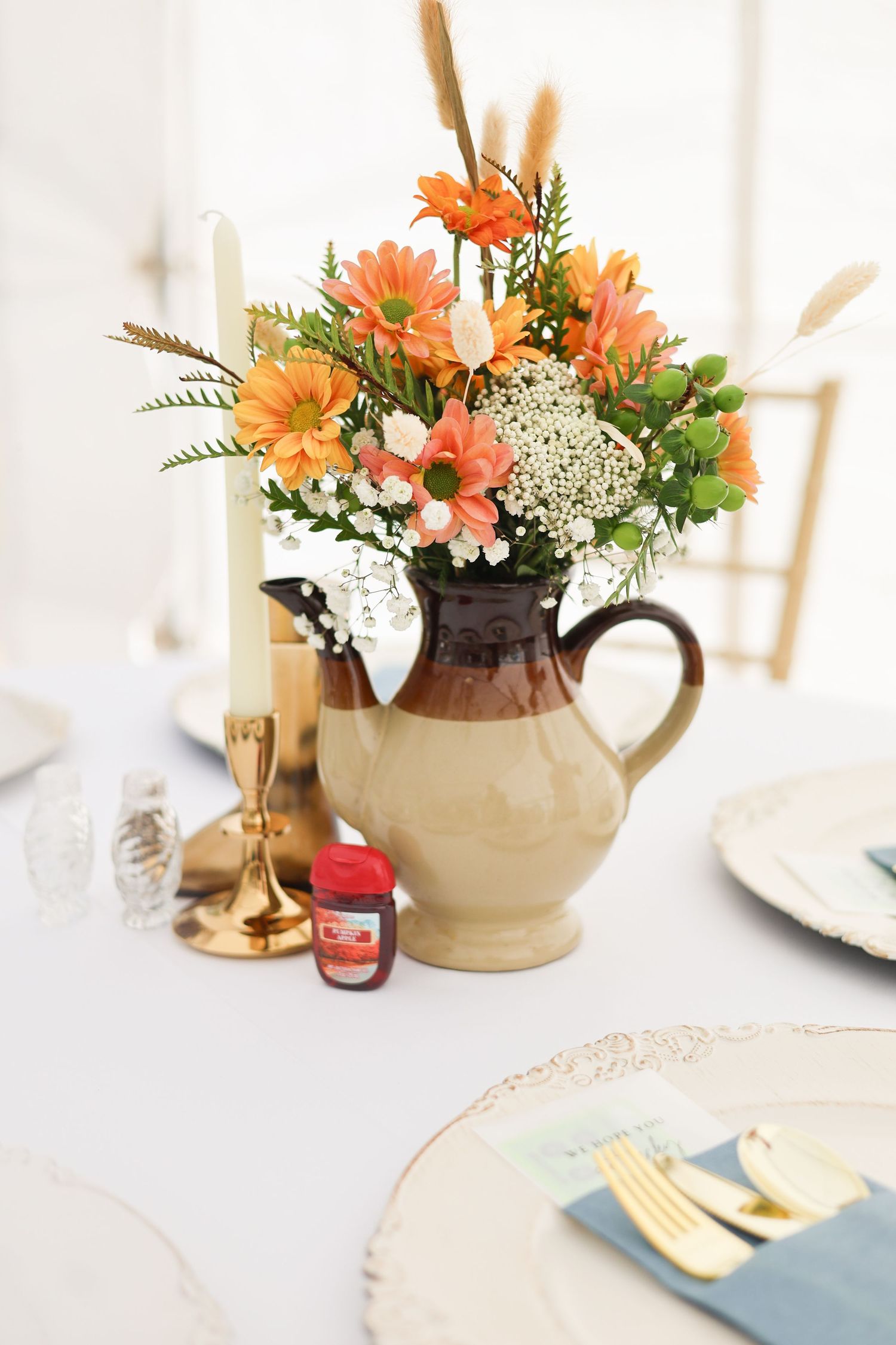 Table setting with orange flowers in teapots and blue napkins with gold flatware.