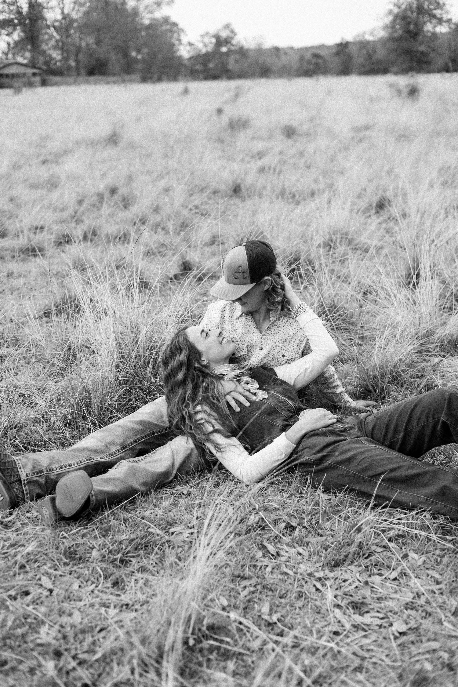 A romantic couple lying together in a grassy field captured in black and white photography.