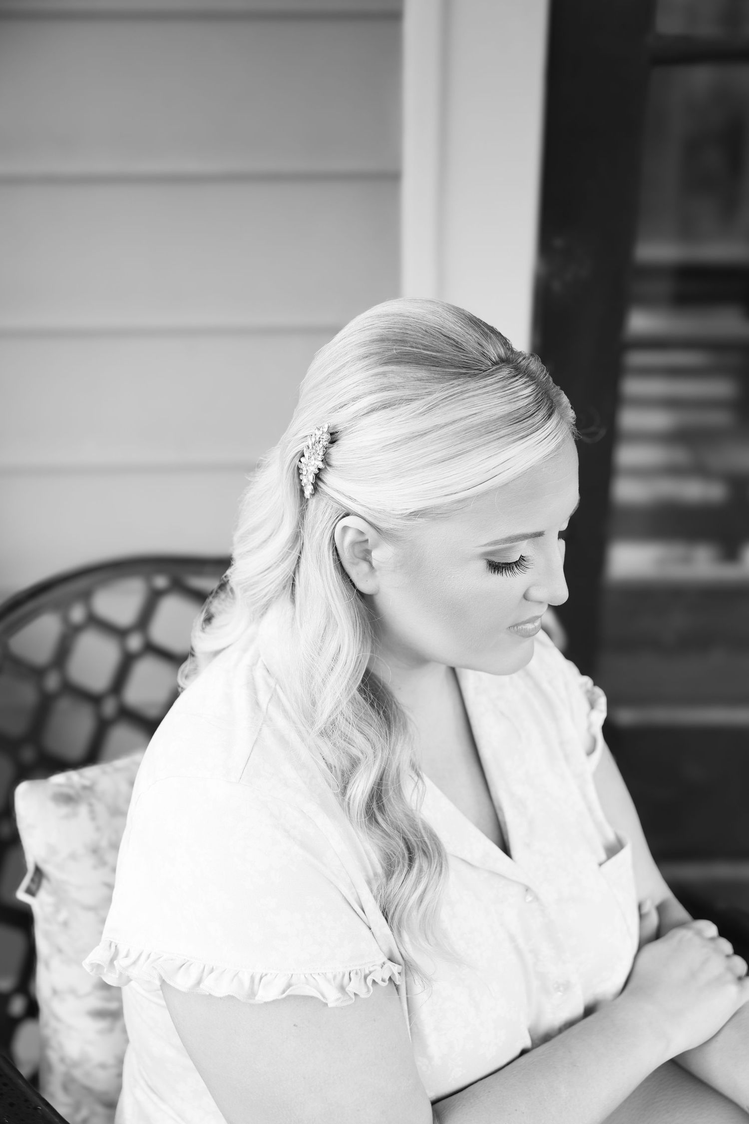 Black and white portrait of a blonde bride with a hair clip, looking down gracefully in a white ruffled top.