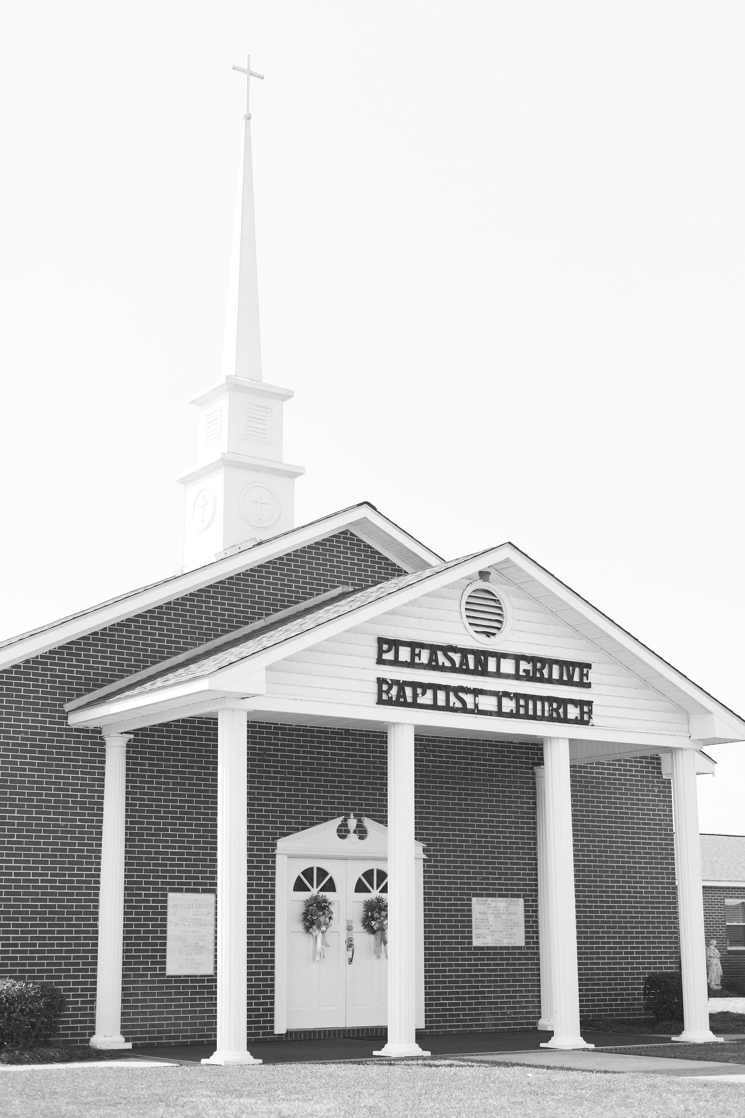 Pleasant Grove Baptist Church exterior featuring brick facade, white columns, steeple with cross, in black and white photography.