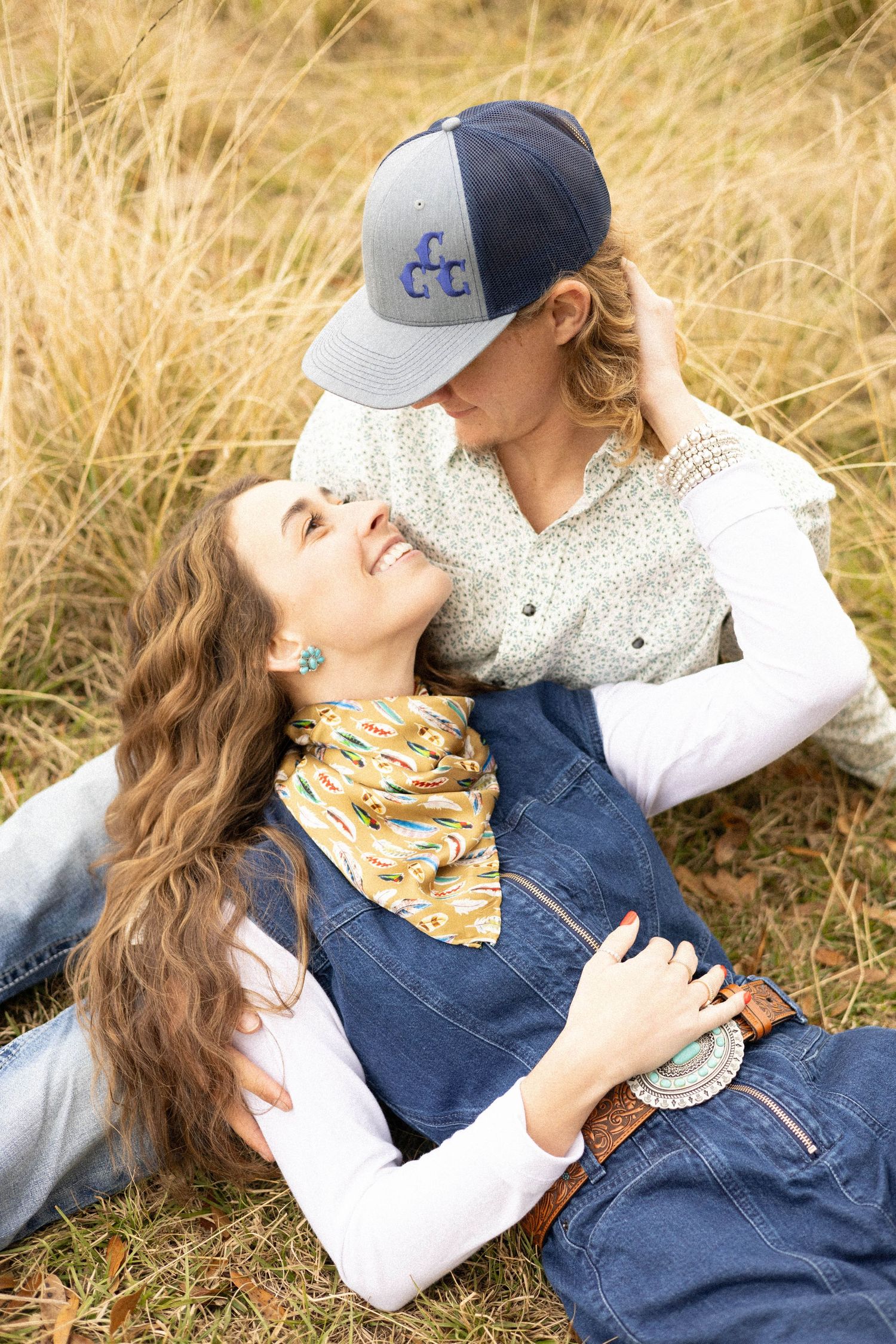 Couple lying in golden grass field wearing casual denim and baseball caps.