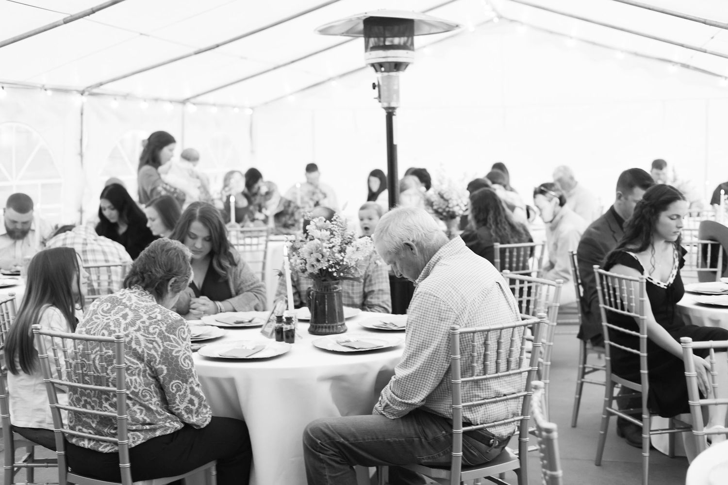 Reception tent with white linens and chiavari chairs set for wedding dinner.