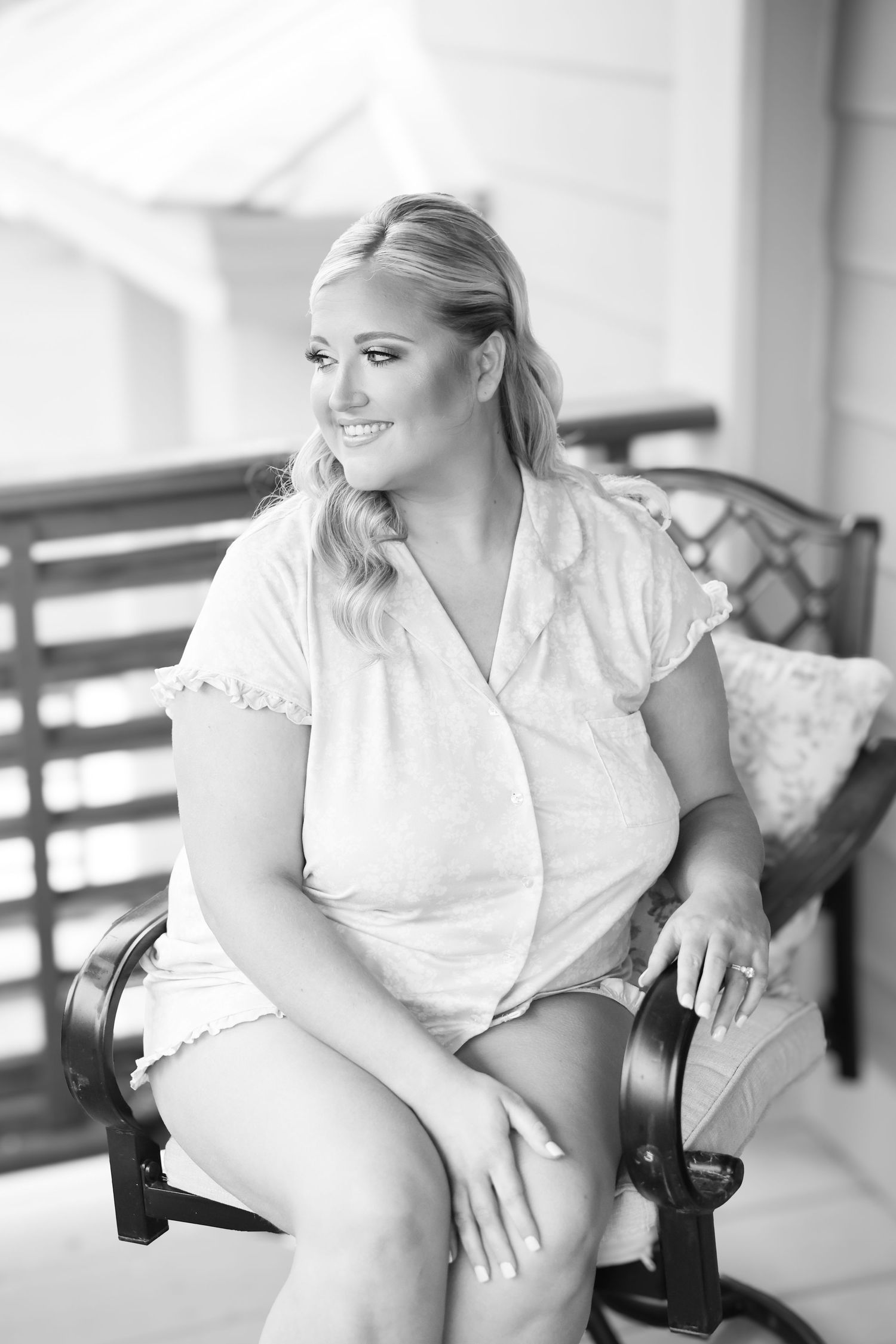 Smiling blonde woman in white dress sitting on bench outdoors in black and white portrait photo.