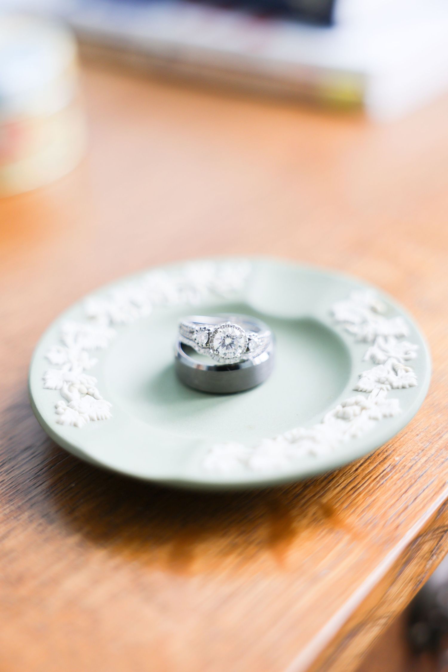 Wedding rings resting on a sage green decorative plate with floral embossing on a wooden surface.