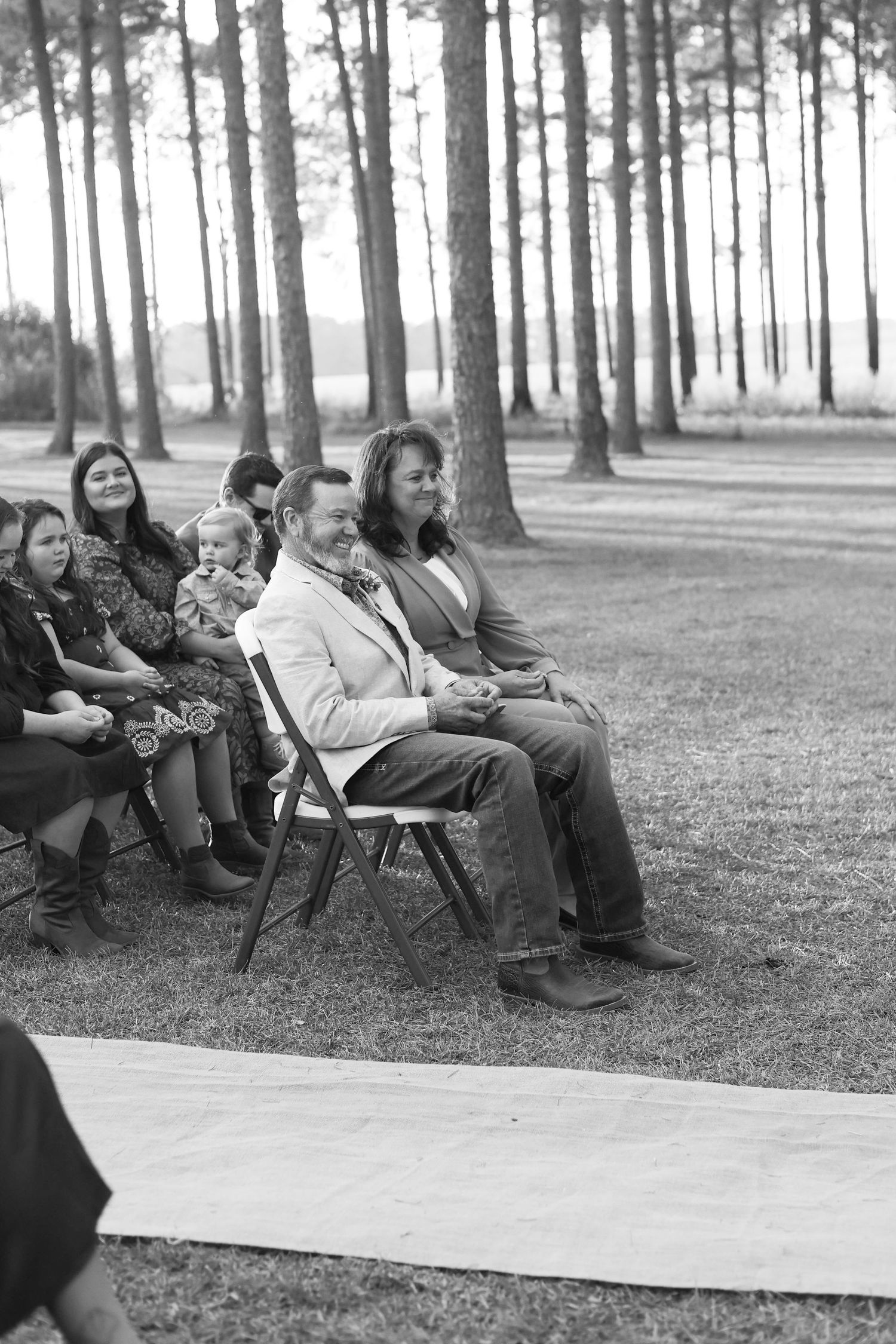 Guests sitting on folding chairs in a wooded outdoor wedding venue.