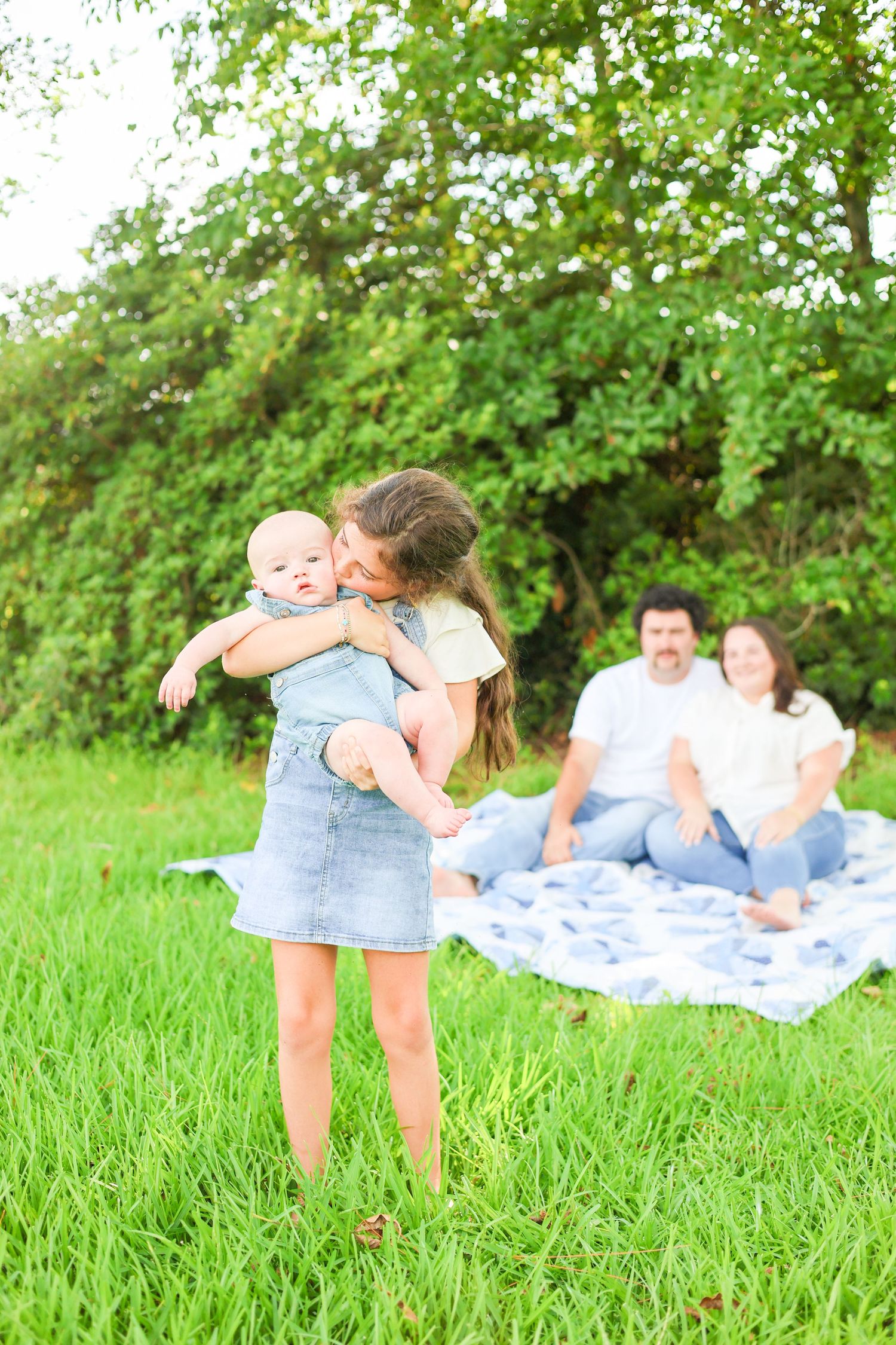Family enjoying playful moments together on a picnic blanket in lush green field.