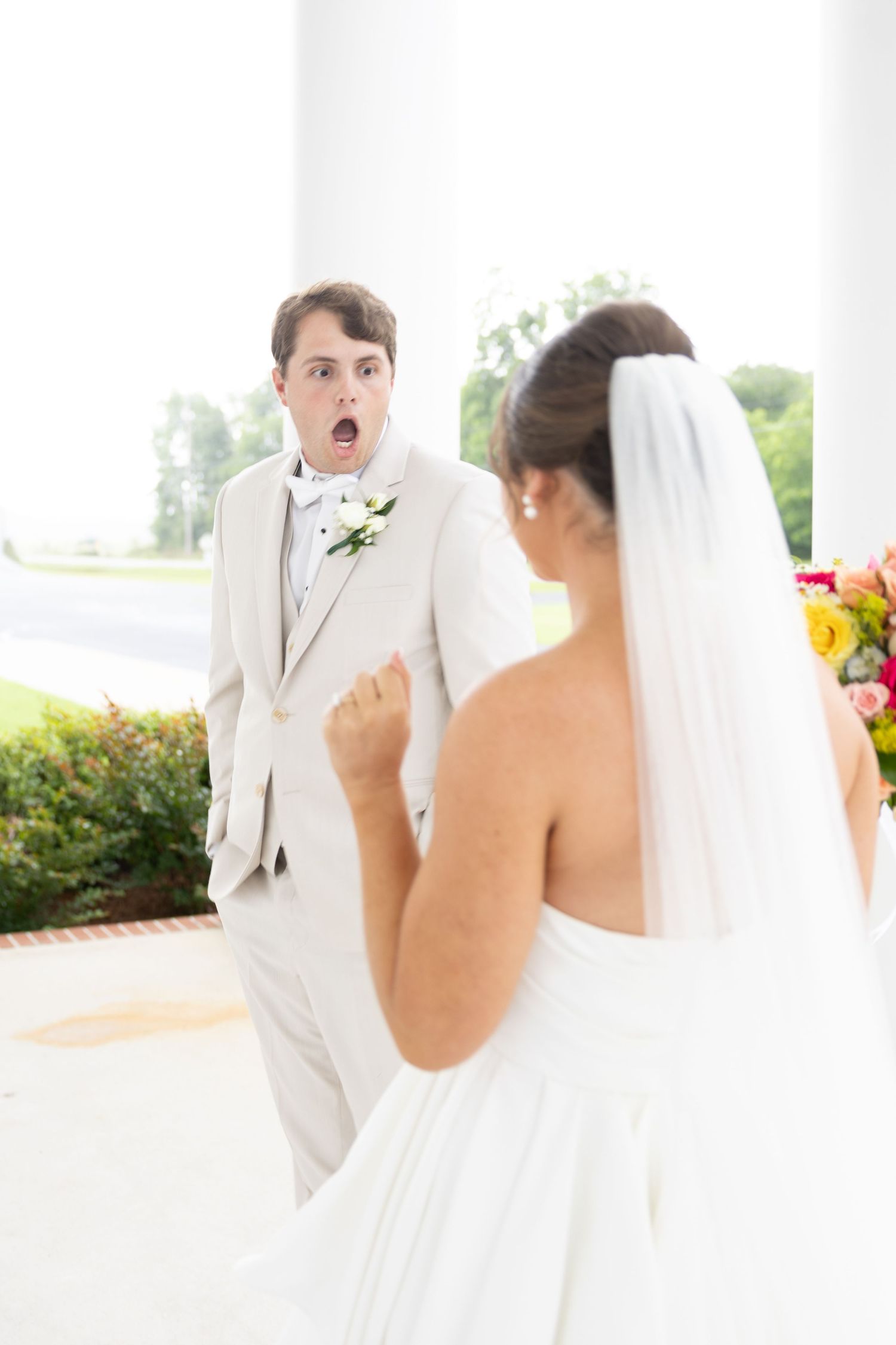 Groom reacts with surprise seeing bride in white wedding dress during first look moment.