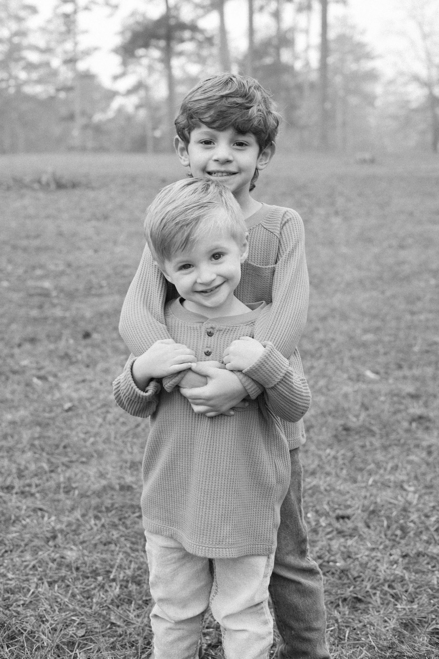 Black and white photo series showing a young child playing and laughing in a grassy outdoor setting.