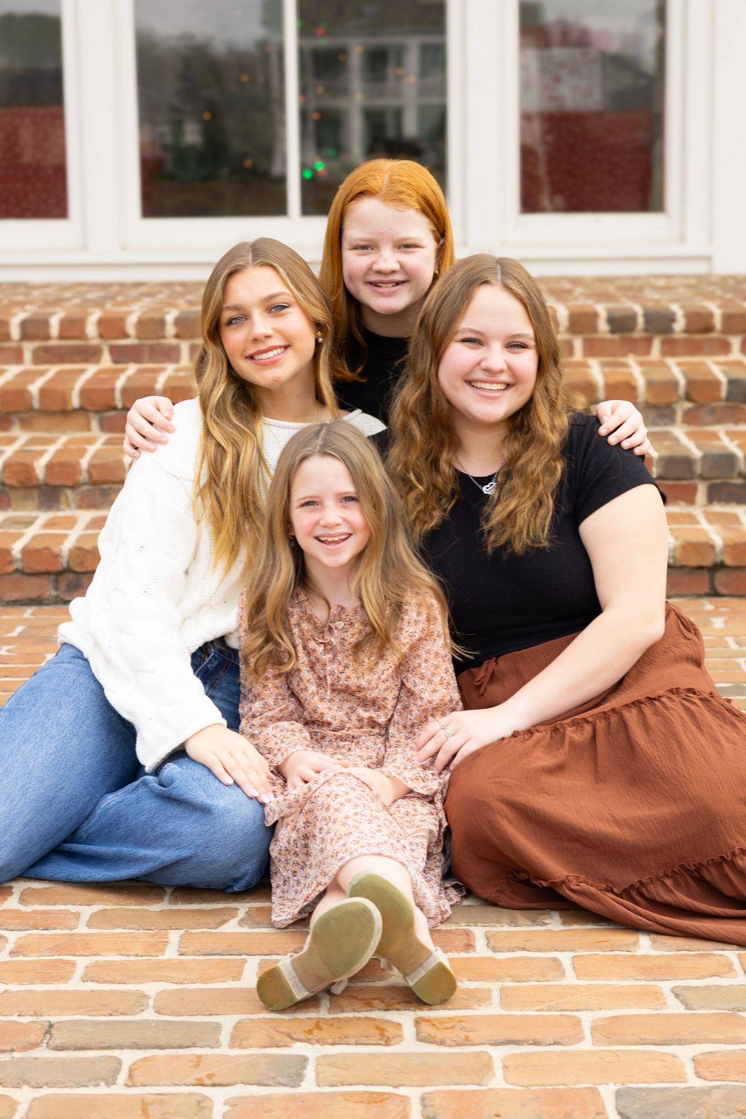 Four young people sitting together on brick steps wearing casual clothing and smiling at the camera.