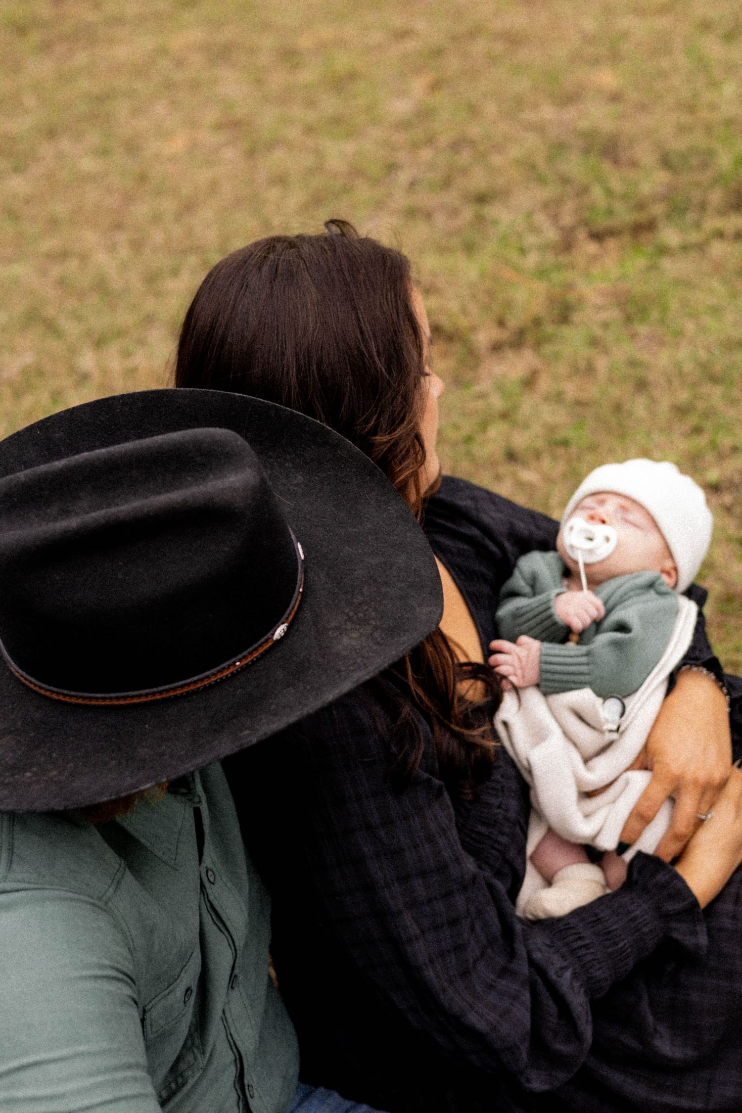 Person wearing black hat holding infant wrapped in light colored blanket.