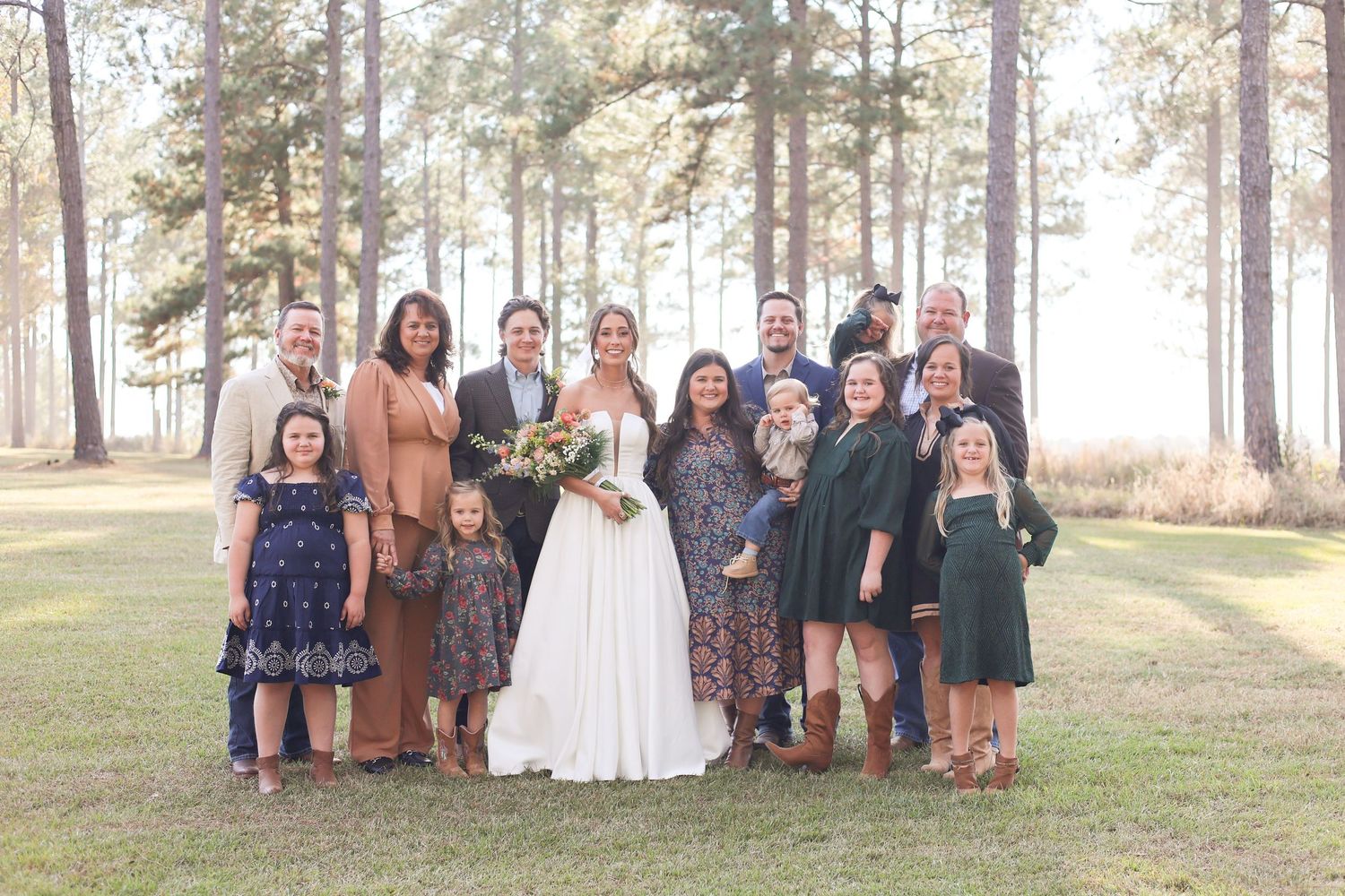 Extended family and wedding party gather for group photo in forest setting.