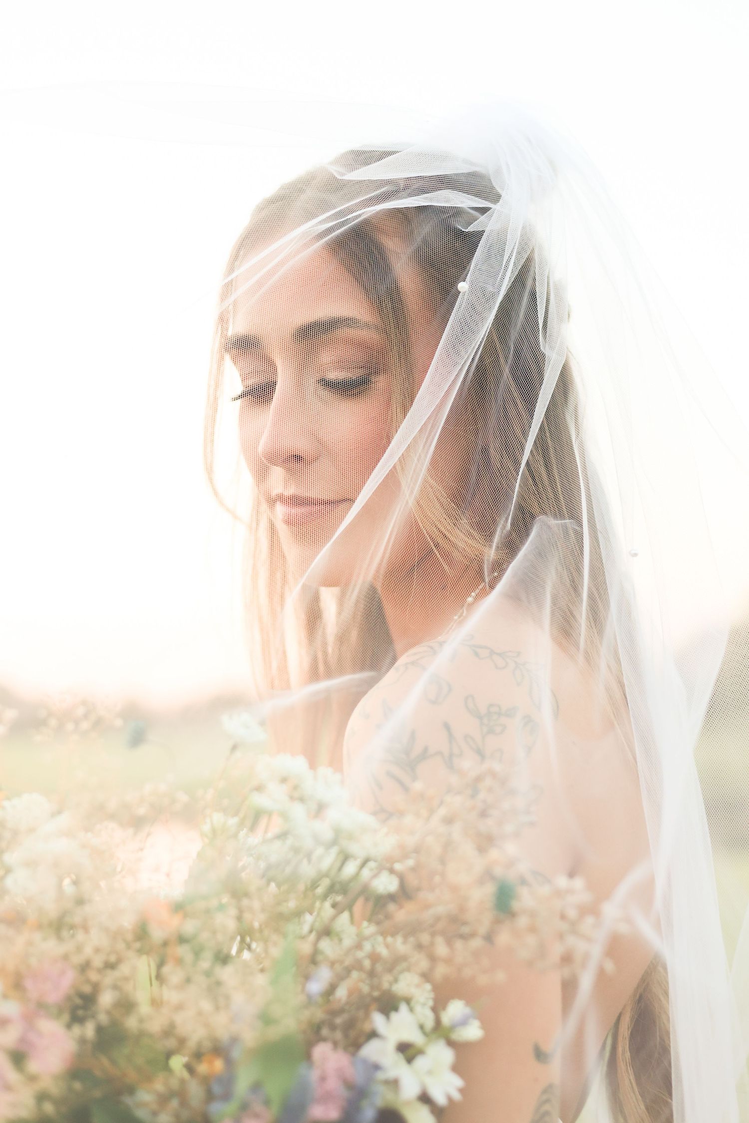 A close-up bridal portrait through a delicate veil with soft natural lighting and wildflowers.