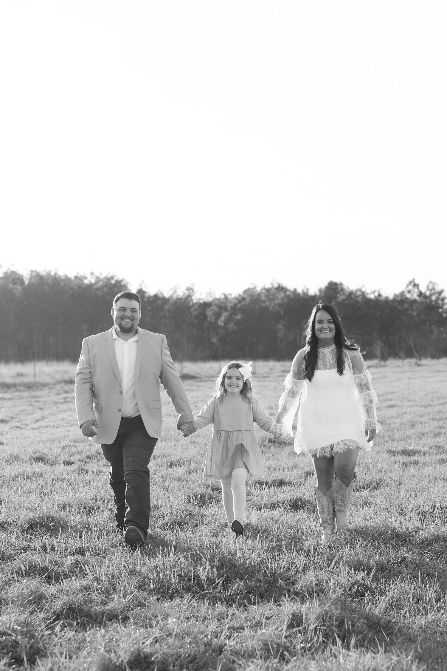 A family walks hand in hand through a sunlit meadow in black and white photography.