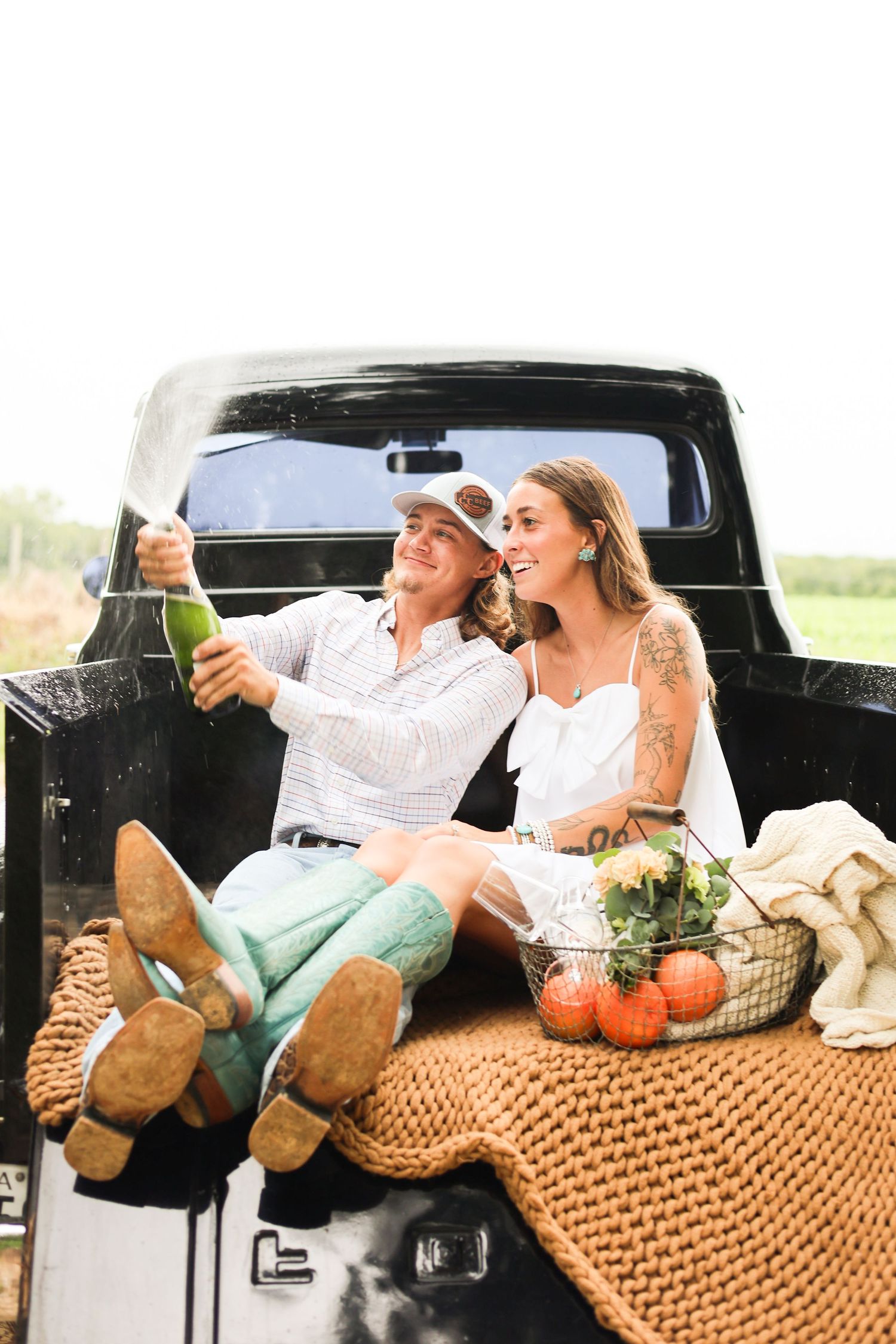 Couple relaxing in truck bed with picnic basket and blanket on sunny day.