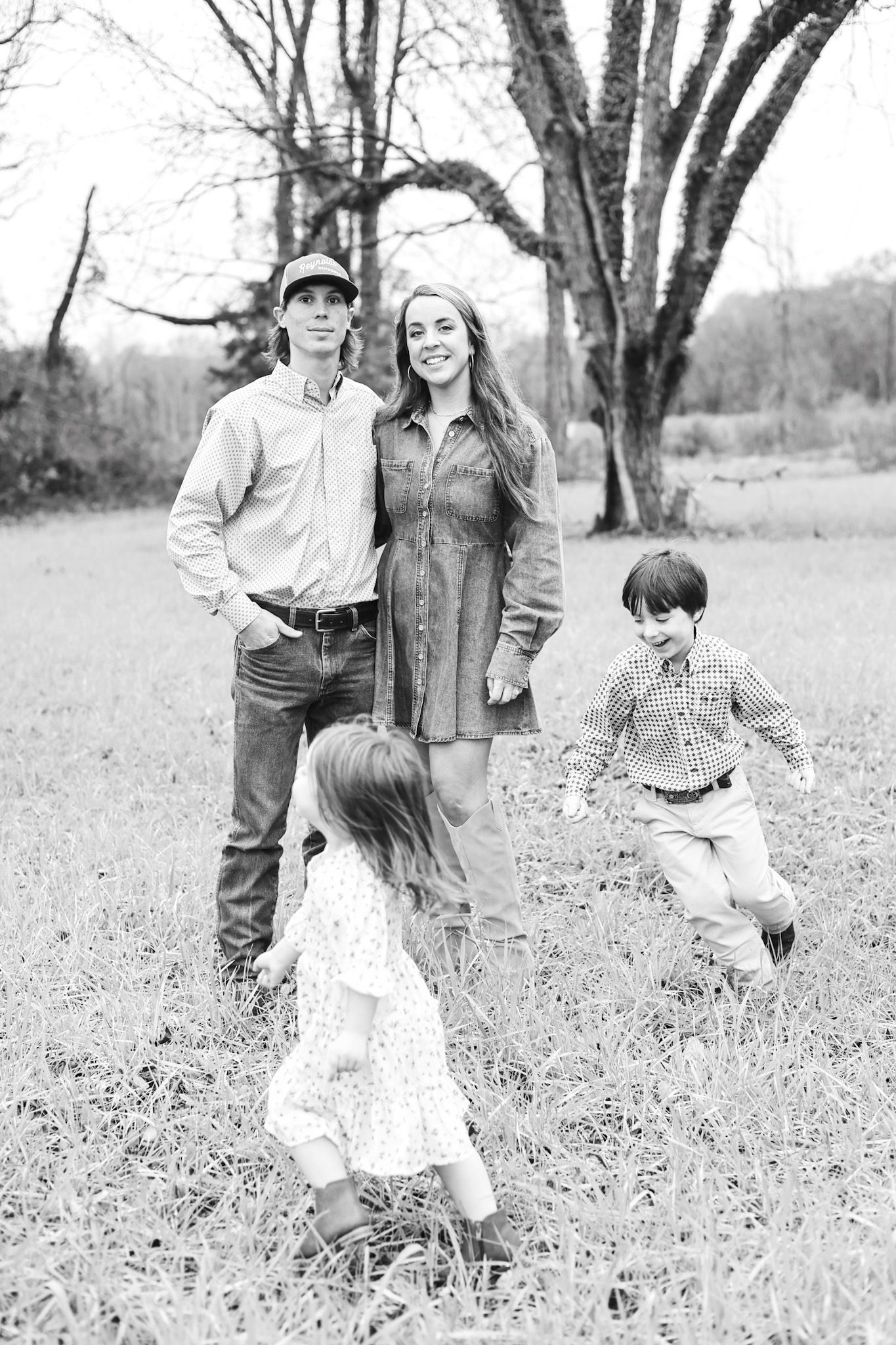 A family enjoys a playful moment together in a rustic field setting captured in black and white.