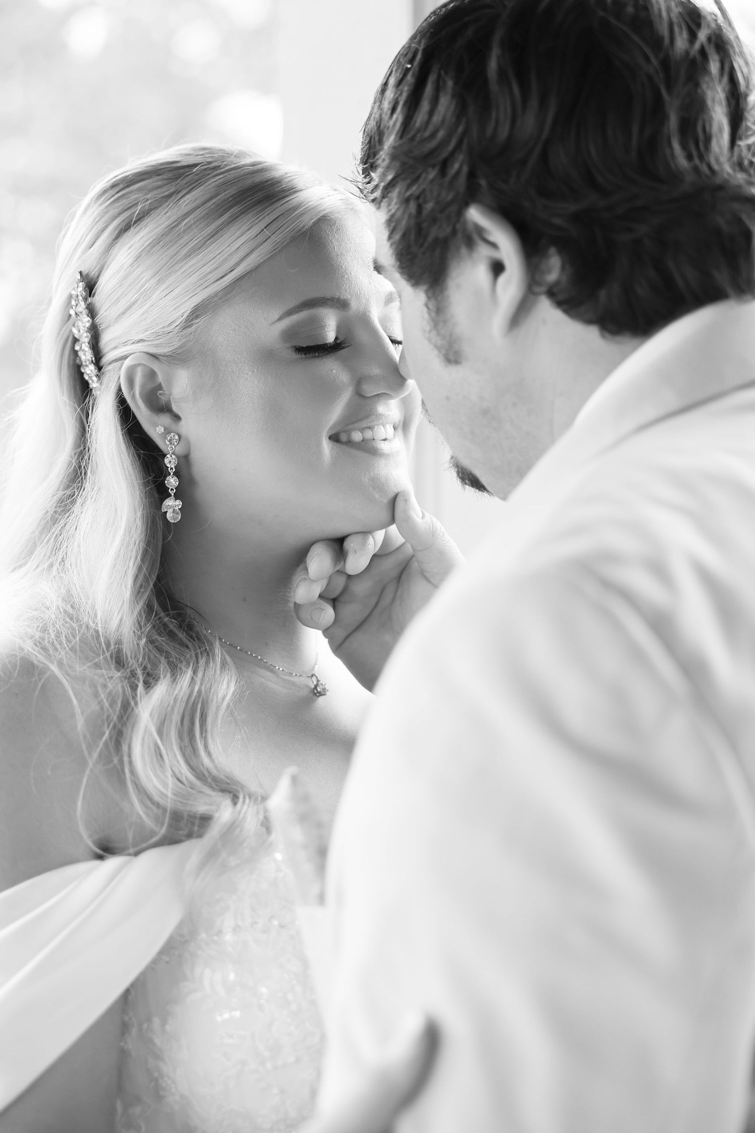 Groom tenderly lifts bride's chin as she smiles with eyes closed in an intimate black and white wedding photo.