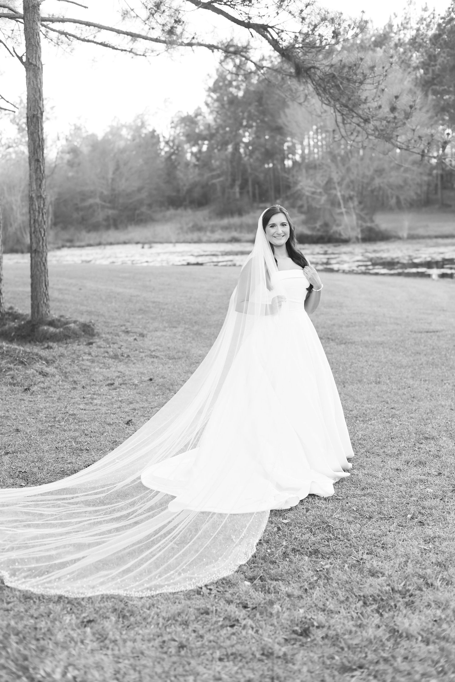 Bride in a flowing white ball gown with a long cathedral veil poses outdoors in a black and white portrait.