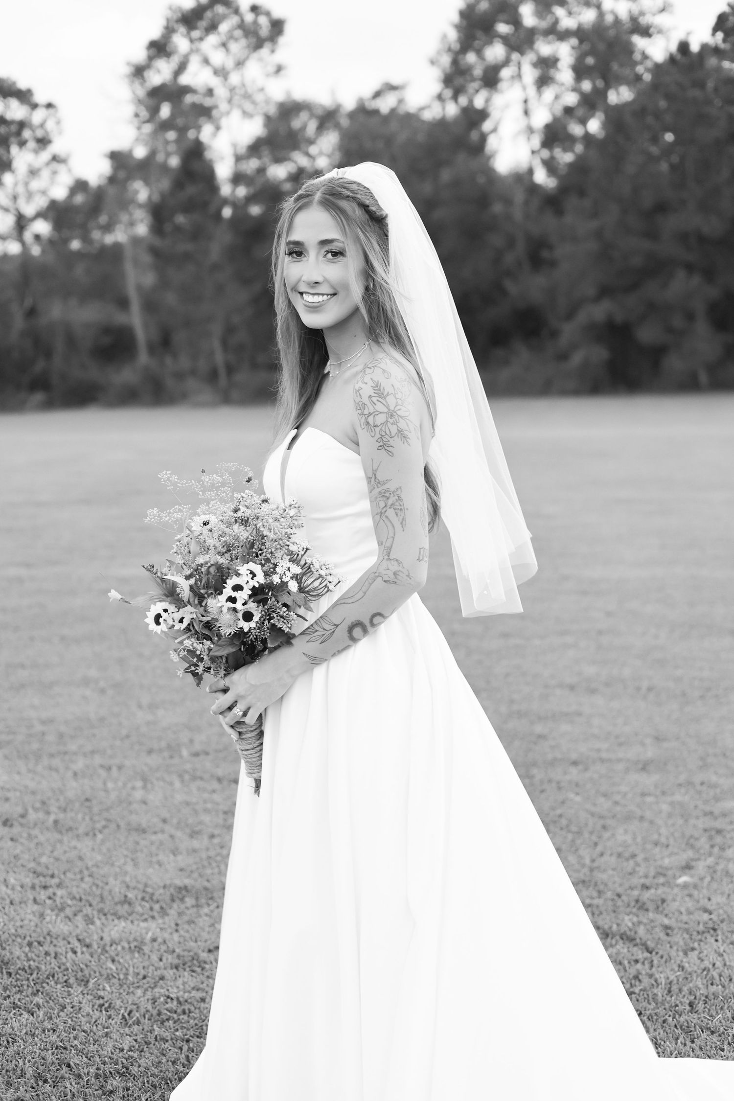 Black and white bridal portrait showing a flowing dress and natural bouquet in an outdoor setting.
