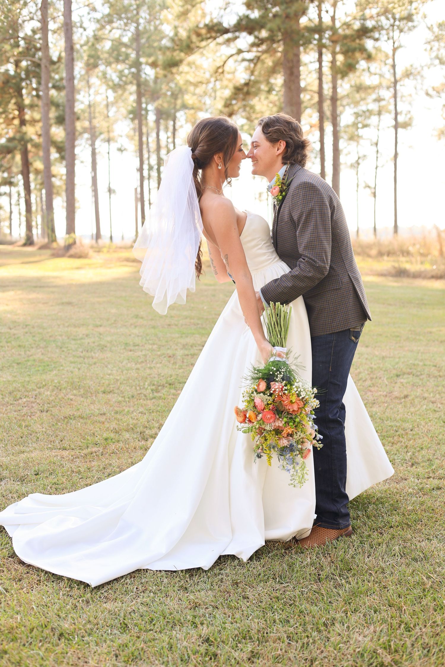 A romantic wedding portrait in a pine forest with warm sunset lighting and a beautiful floral bouquet.