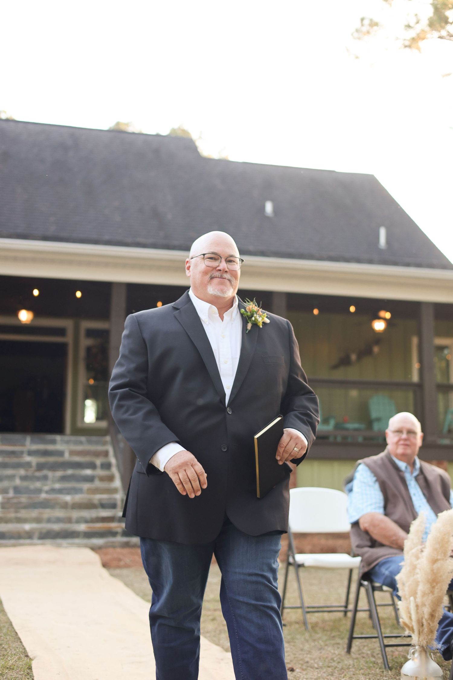 Wedding party members in formal attire gather outside a venue with string lights.