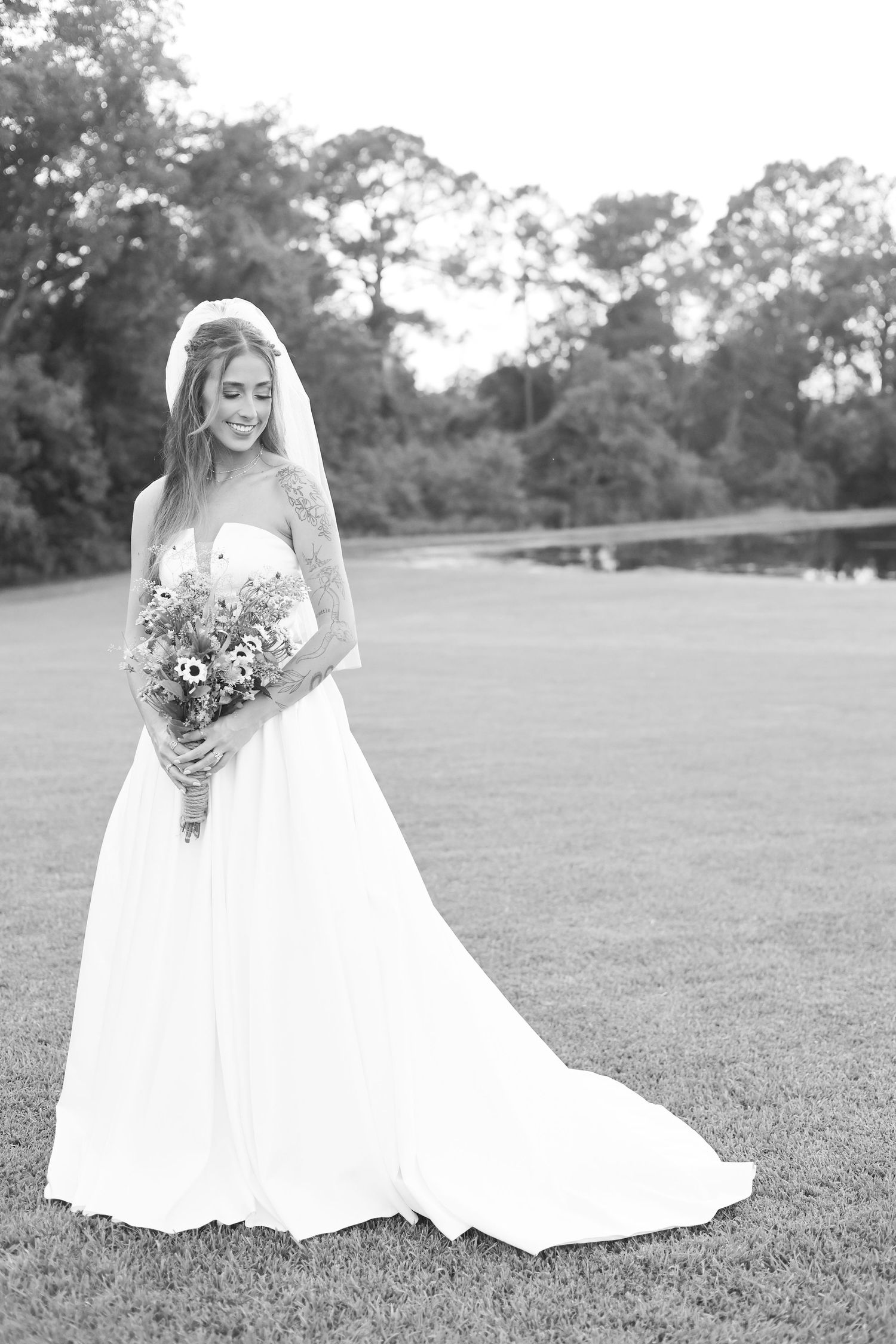 Black and white wedding photo of a bride with her bouquet in a grassy field.