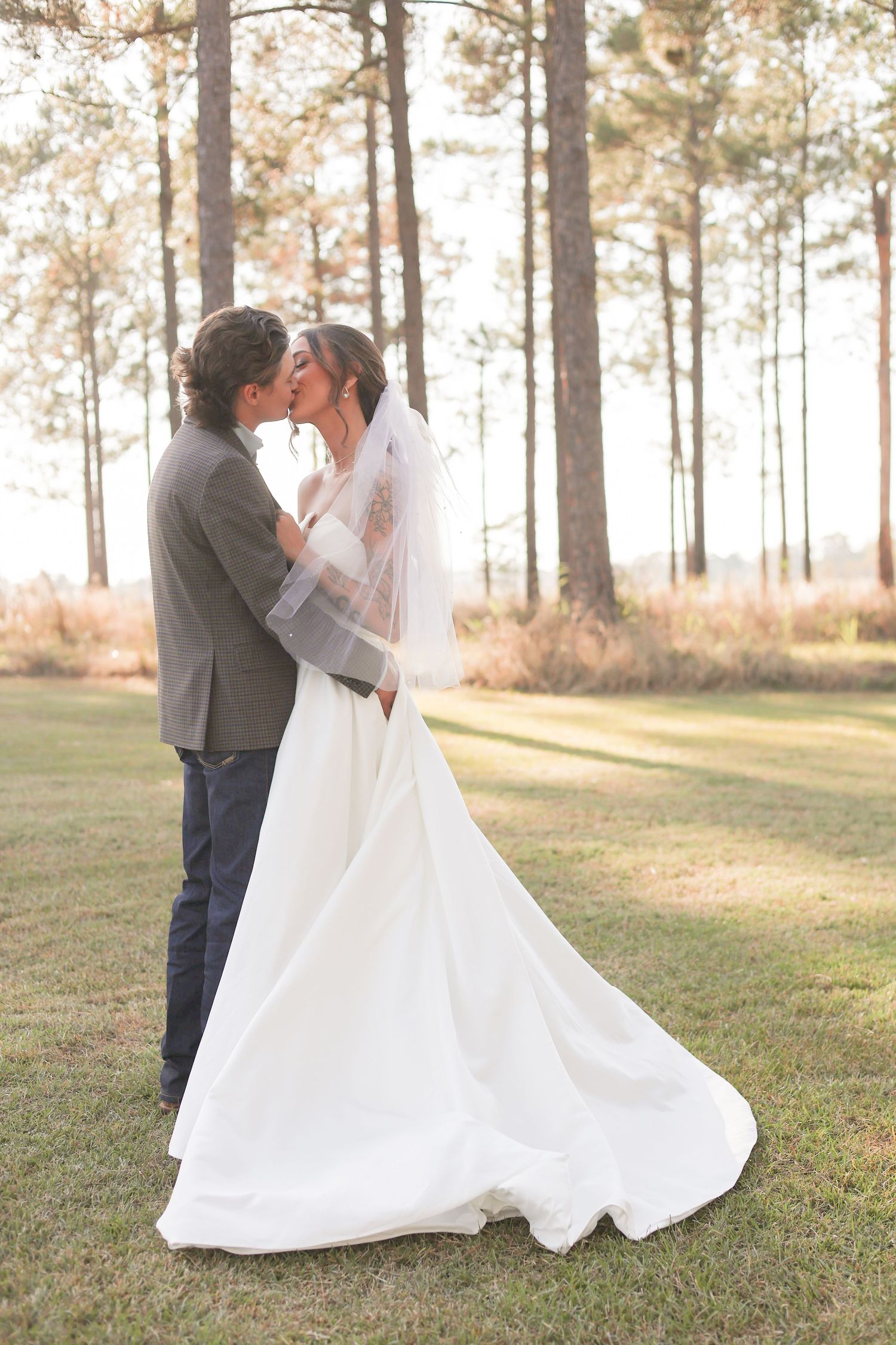 An intimate wedding embrace captured against a backdrop of tall pine trees at sunset.