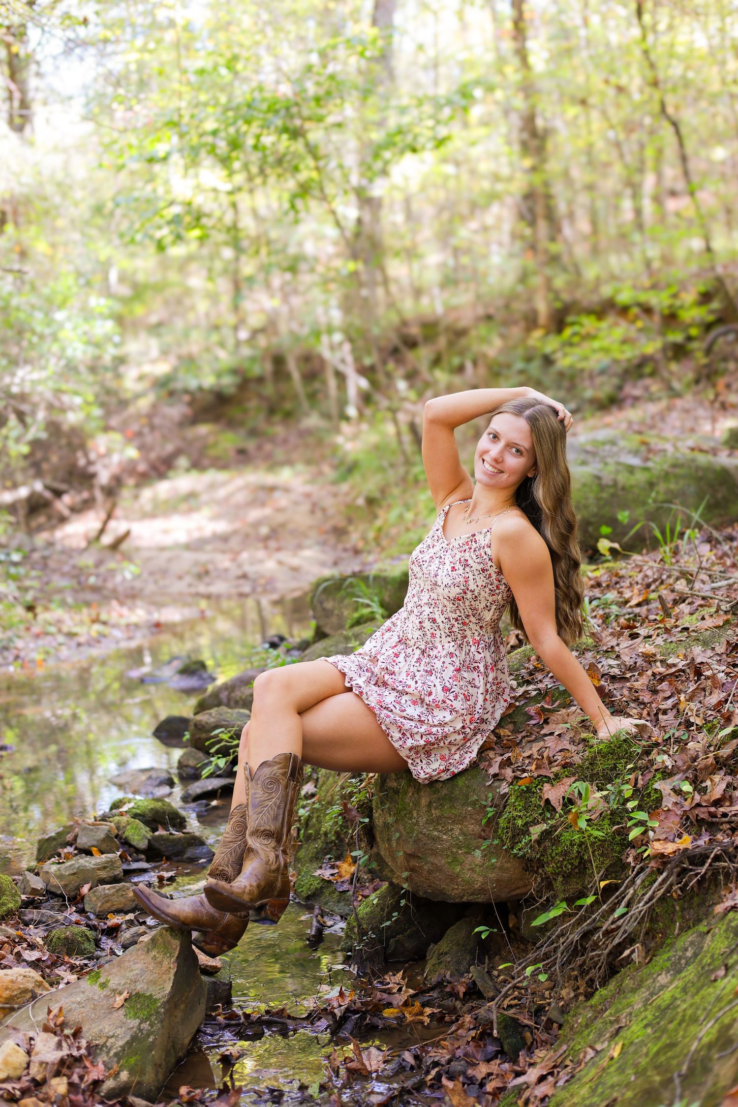 A floral dress and brown boots create a rustic look against a mossy creek backdrop in a woodland setting.