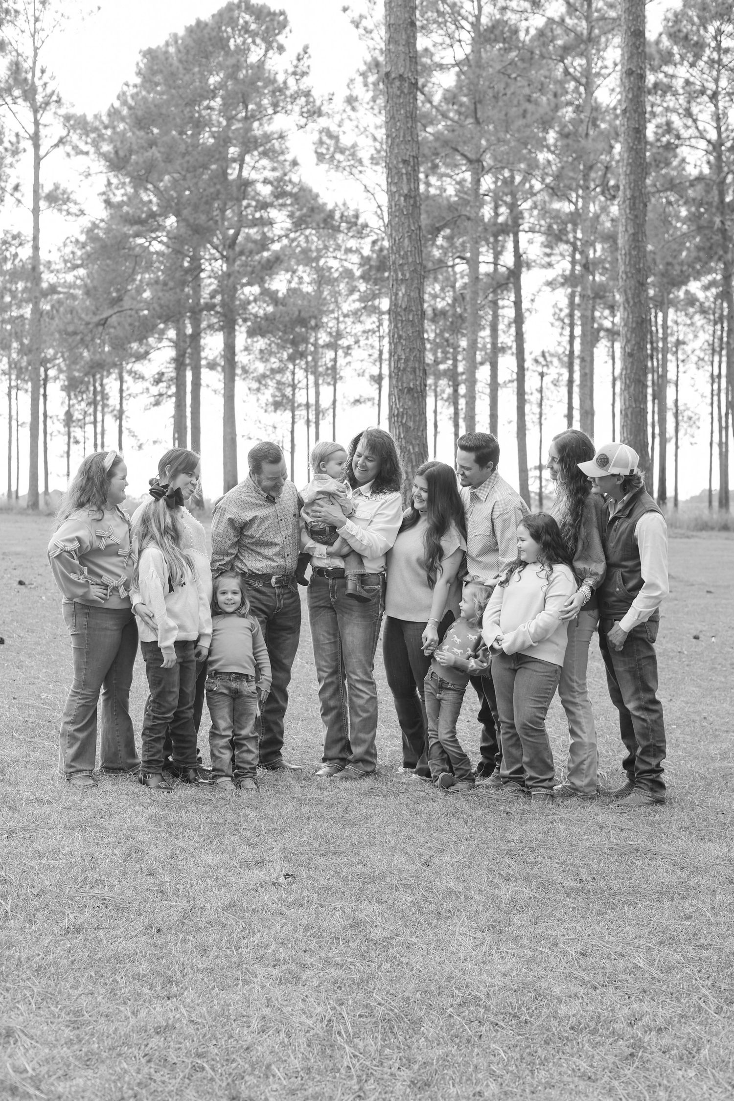 People standing in a line on a grassy slope with pine trees in the background, captured in monochrome.