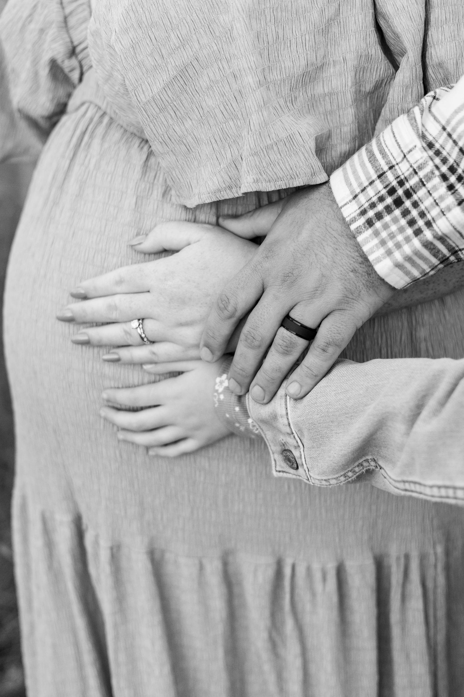 Black and white photo of a pregnant woman, partner, and child's hands resting on her baby bump.