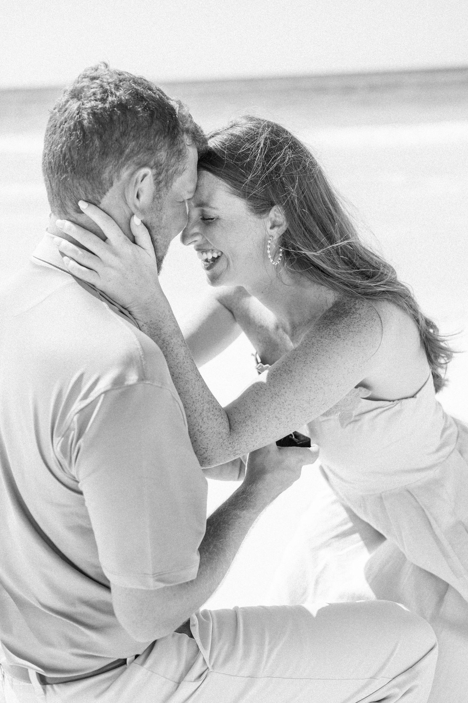 Black and white photo of a happy couple embracing and laughing together on a beach.