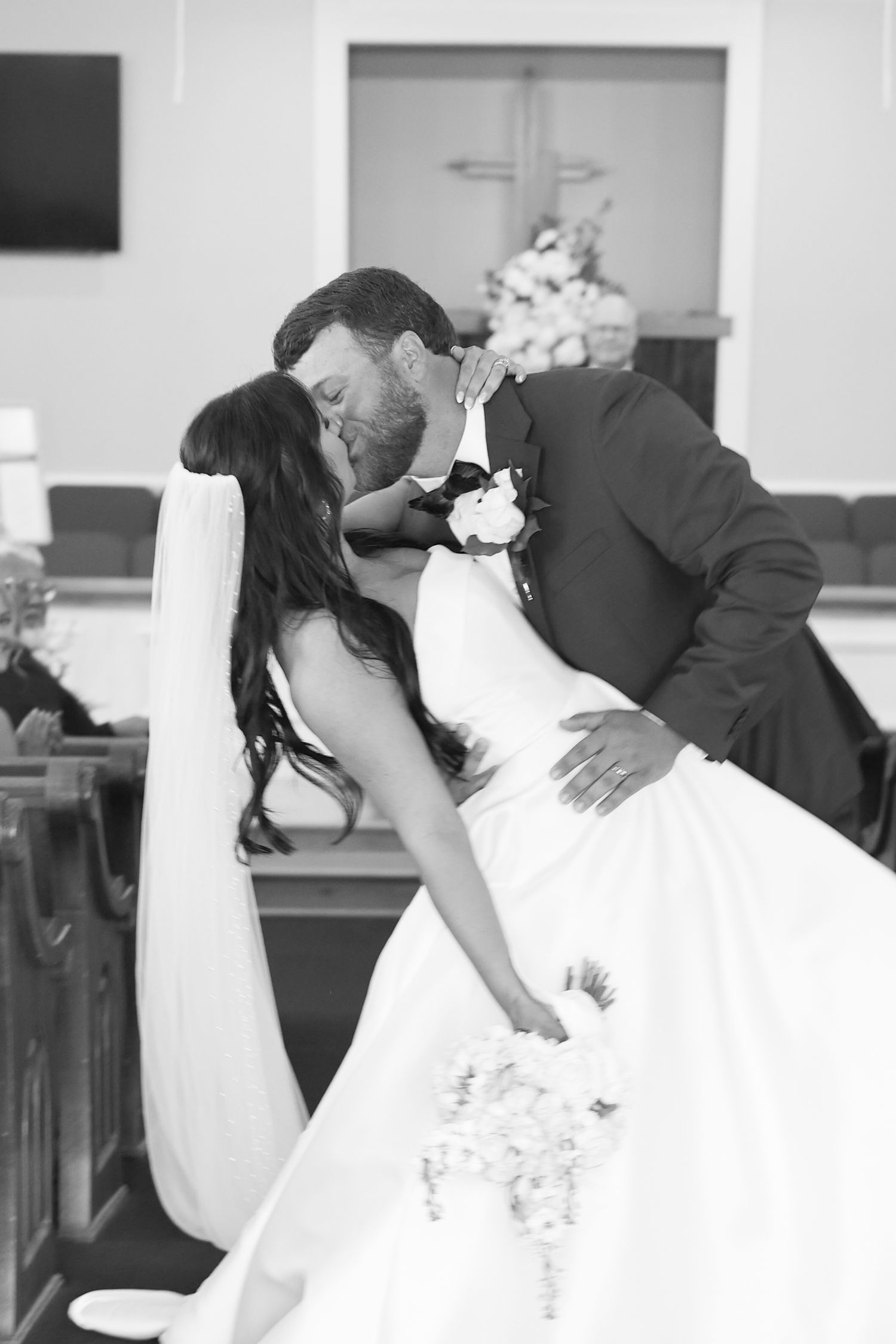 Black and white photo of a groom dipping and kissing his bride in a church after their wedding ceremony.